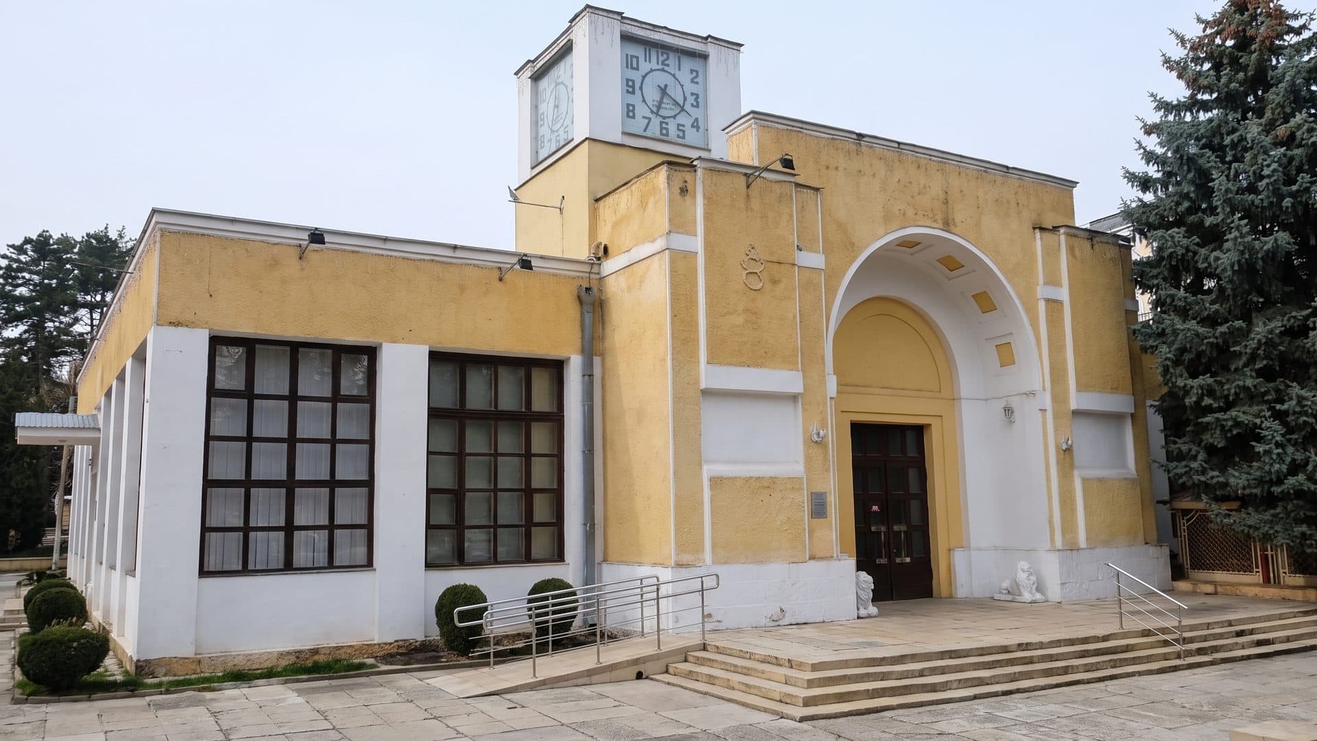 The ochre bath house of the Kislovodsk narzan baths seen obliquely from the corner, stone lions flanking its arch