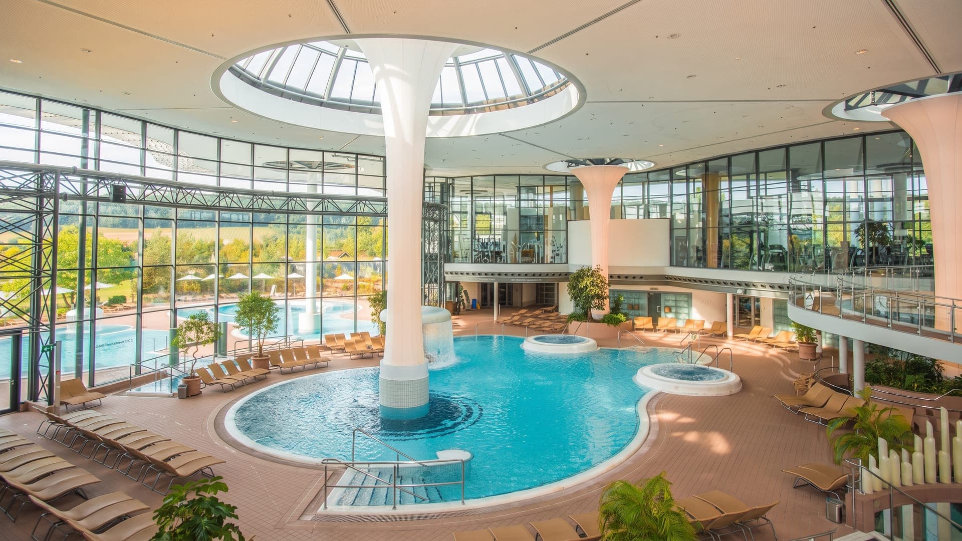Indoor pool under white mushroom columns and a round glass roof light