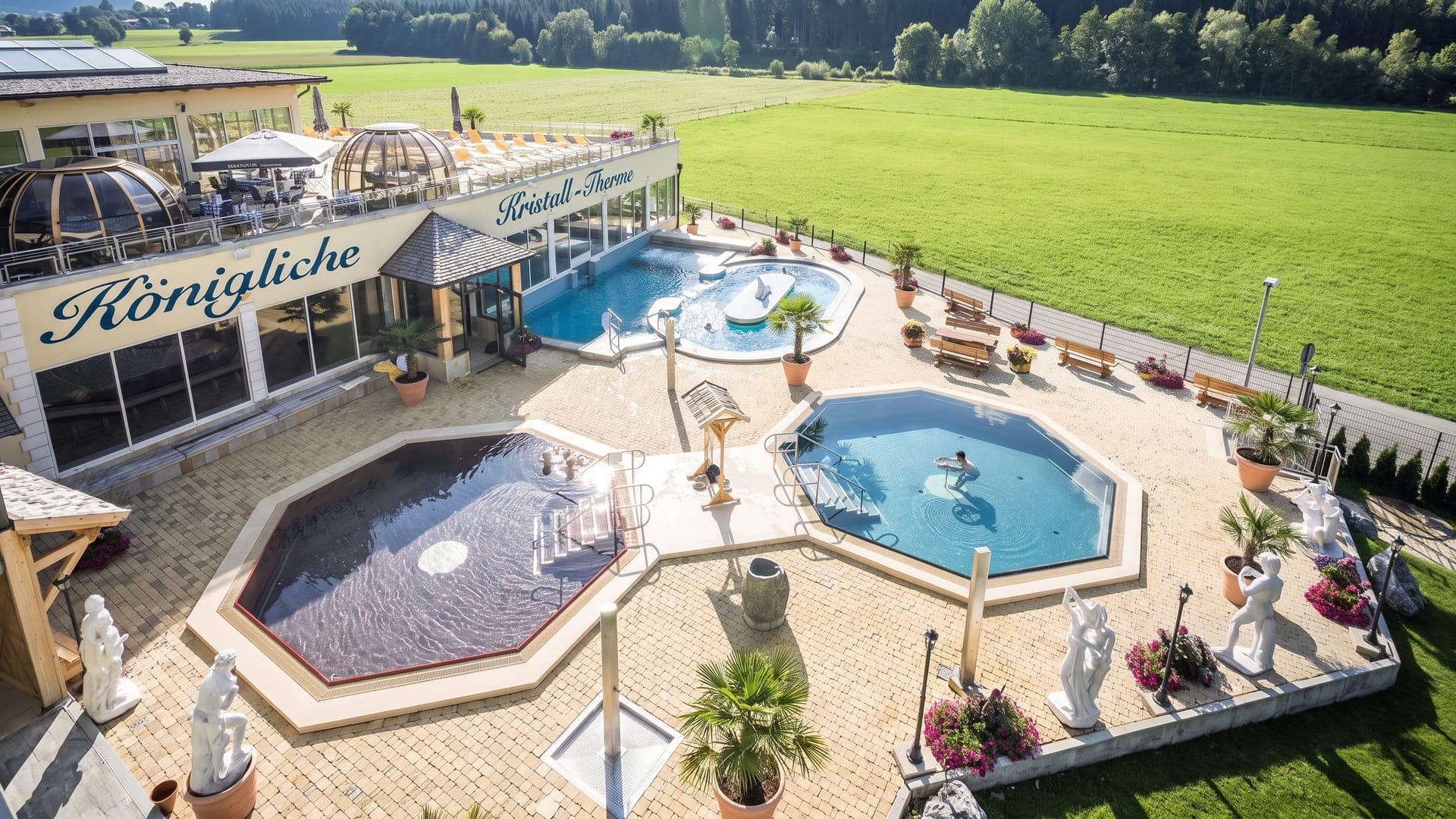 Octagonal outdoor pools on the terrace of the Koenigliche Kristall-Therme in Schwangau, with meadows and wooded hills behind.