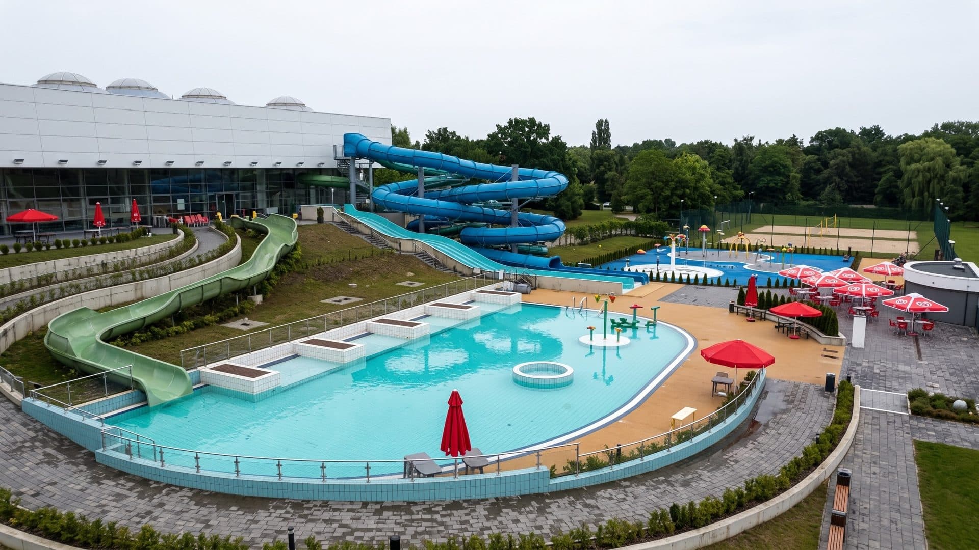 The outdoor pool of the Wodny Swiat complex in Przemysl with blue and green slides down a grassy slope