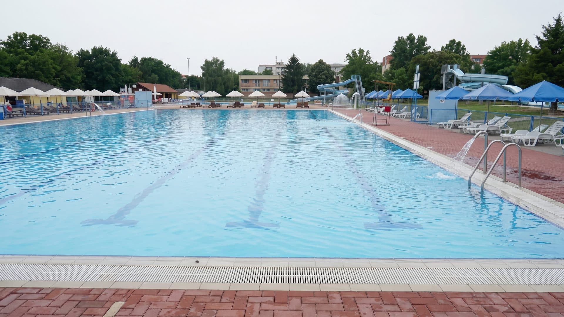 The long outdoor pool at Margita-Ilona with lane markings, a red-paved surround and rows of parasols and loungers along both sides