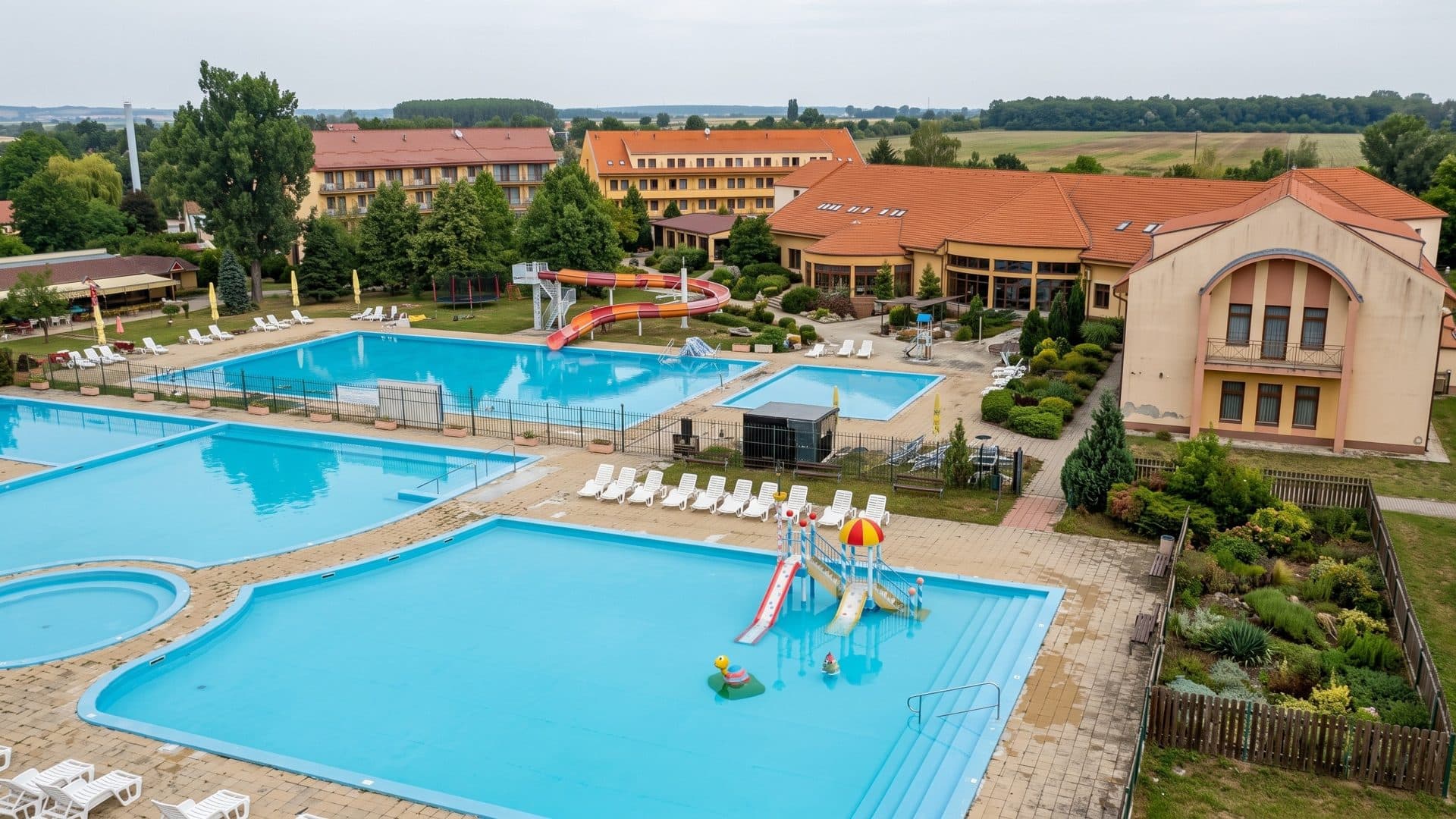 Outdoor pools of the Patince lido with a children's slide, the red-roofed hotel behind