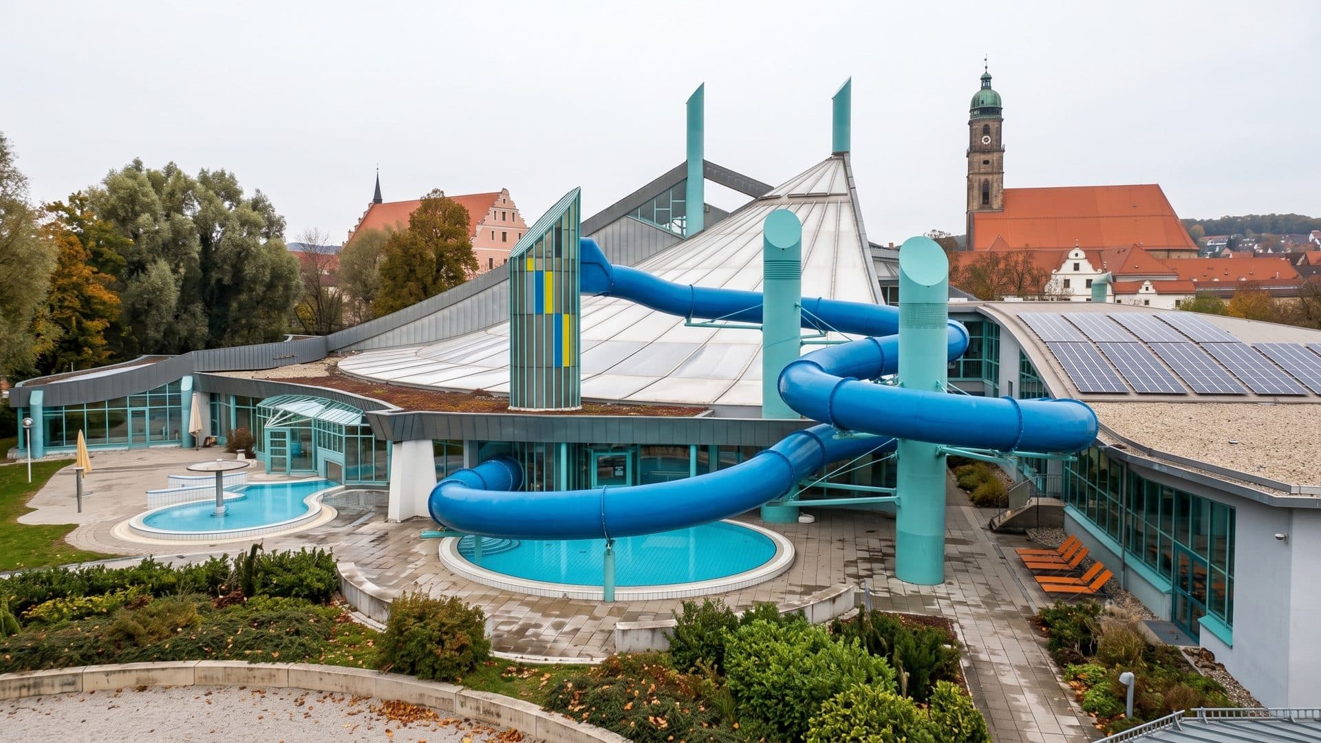 The Kurfurstenbad in Amberg with blue slides and an outdoor pool, the old town church towers behind
