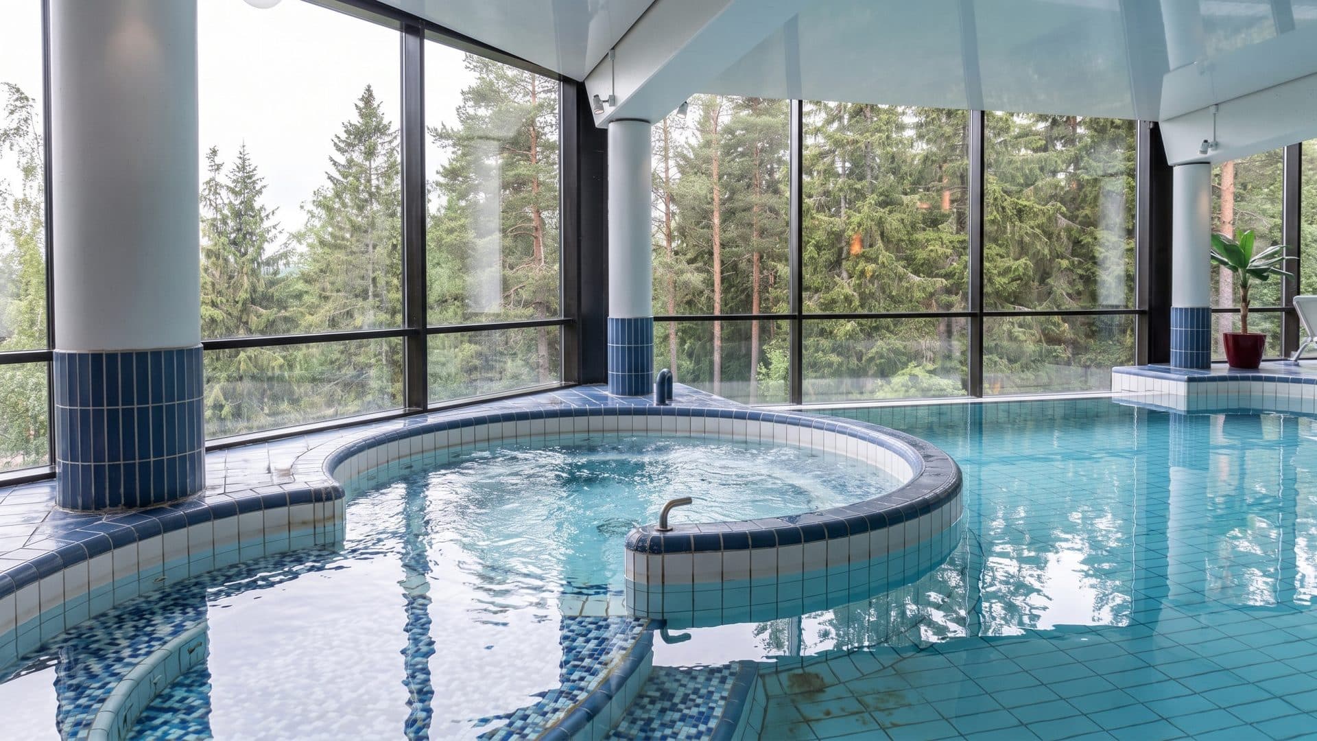 The round whirlpool basin at Kylpyla Laajavuori set into the tiled pool, with pines filling the glass wall behind