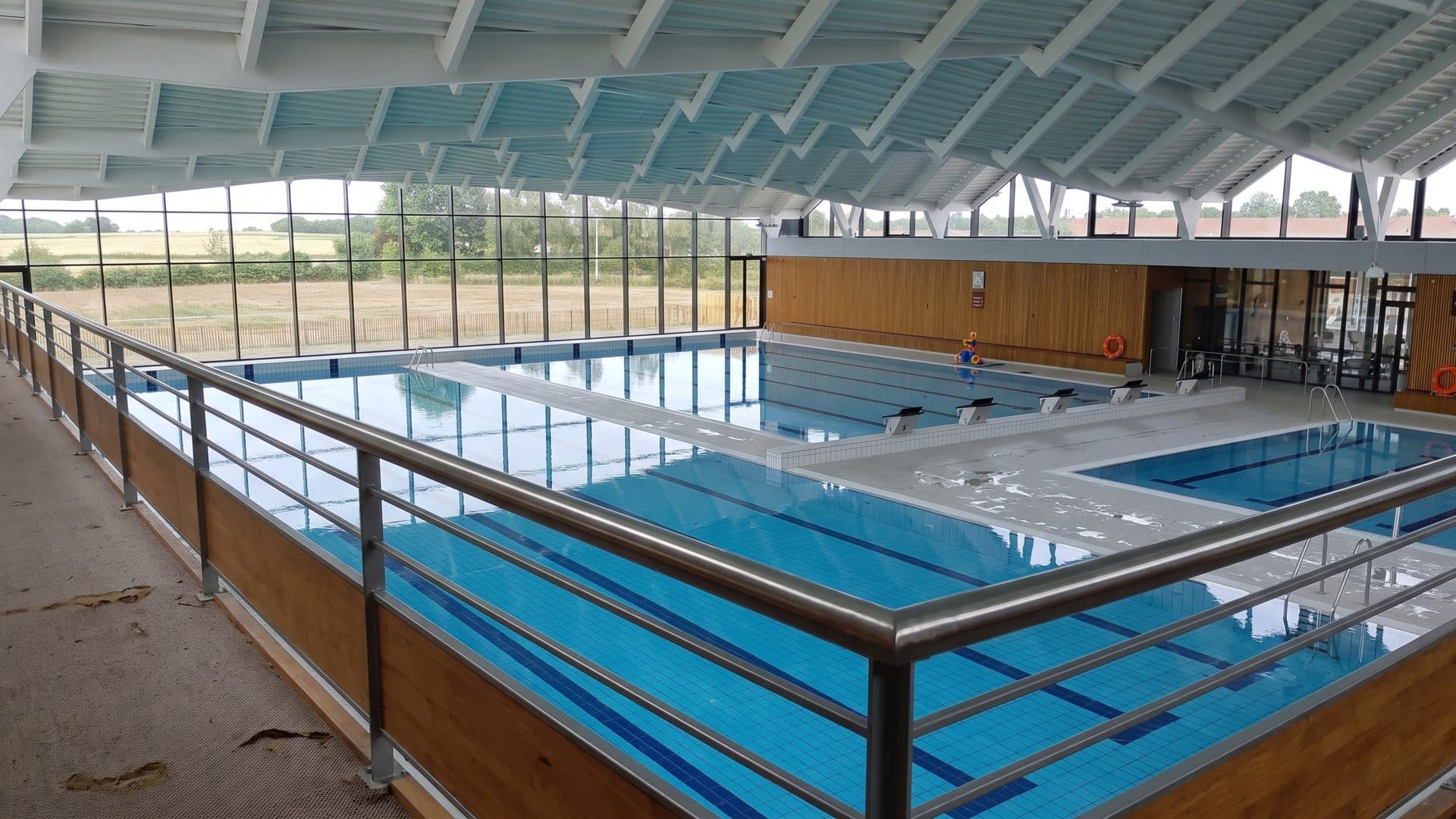 The indoor pools of L'Aqualud in Bergerac seen past a railing, a glazed wall onto the fields