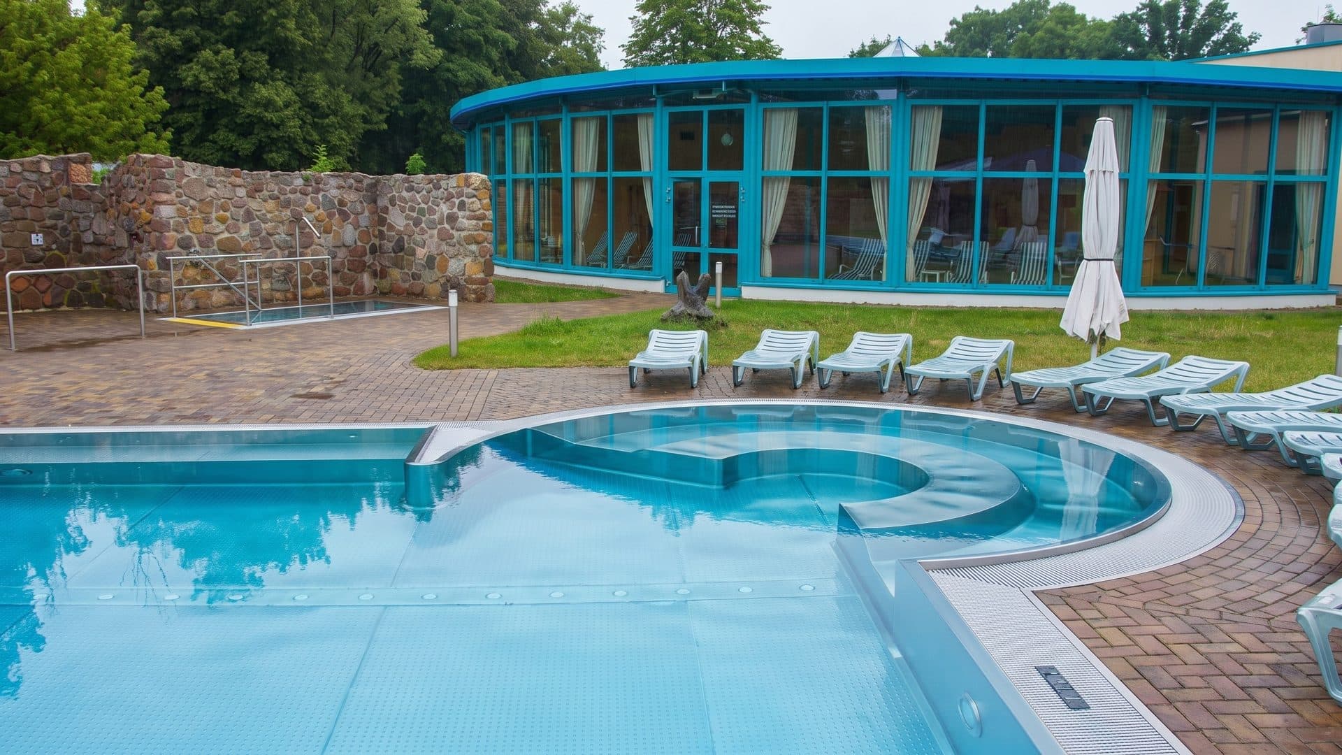 Outdoor thermal pool with a round whirlpool, loungers on the lawn and the round glazed pavilion