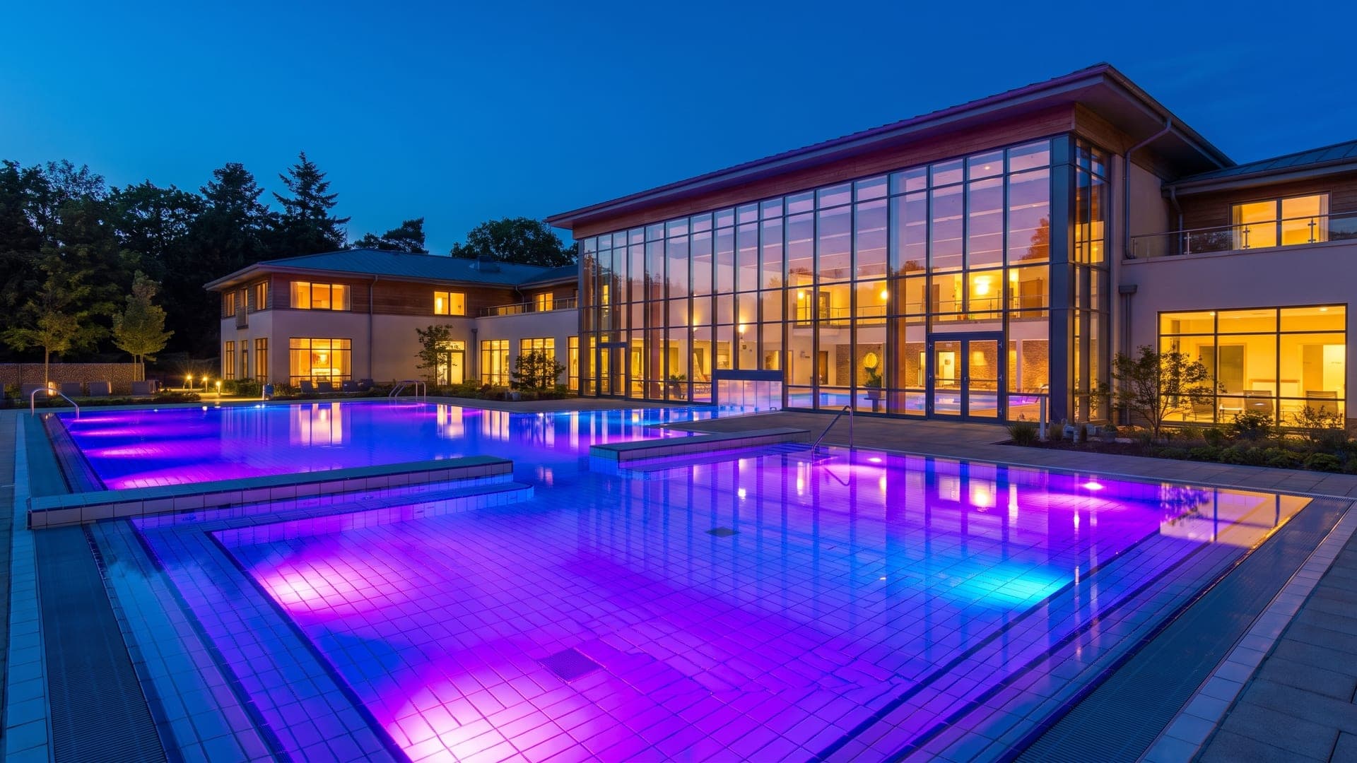 The outdoor pool at the Landgrafen-Therme in Bad Nenndorf at dusk, lit violet and blue in front of the glazed hall.