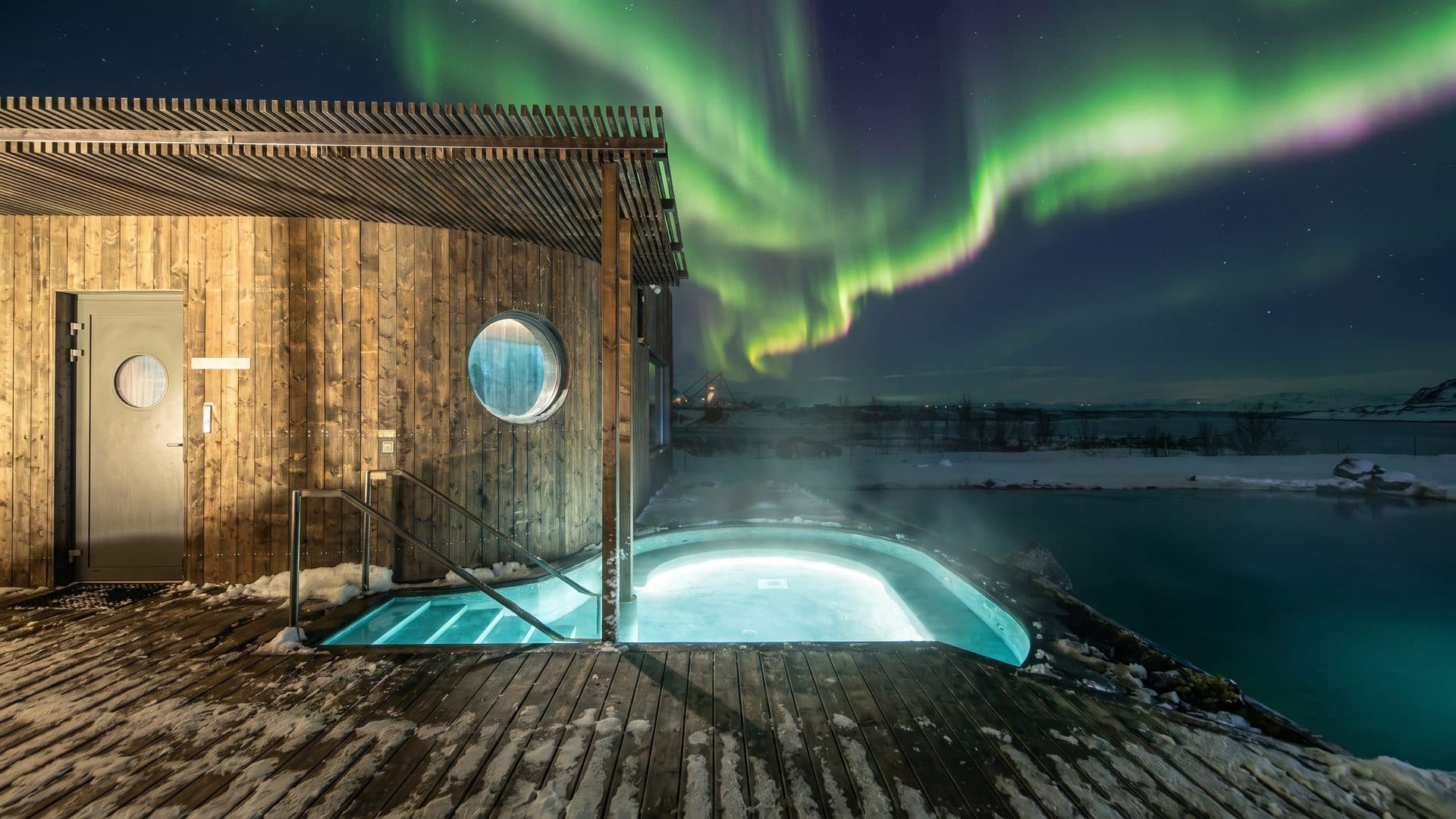 The timber bath house of the Laugaras lagoon with its steaming hot pool under the aurora