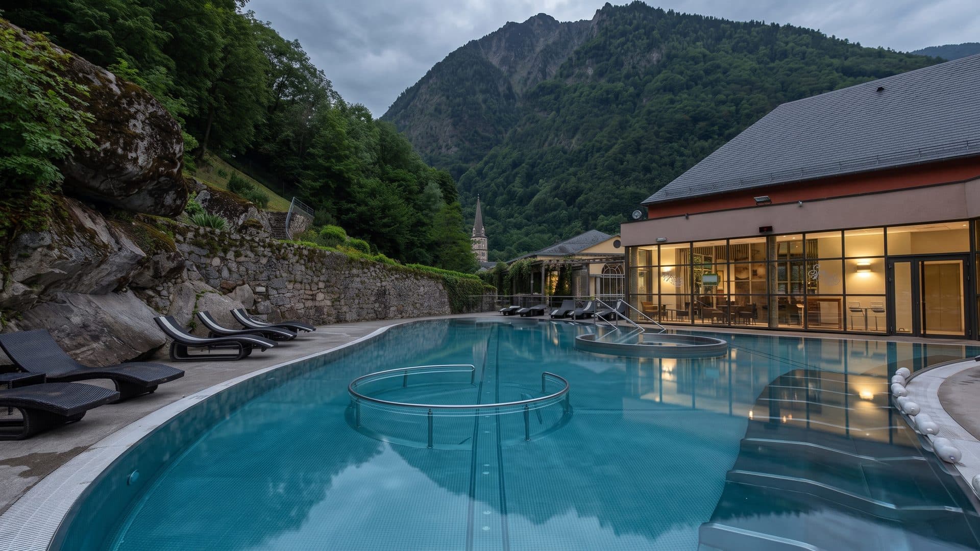 The outdoor thermal pool of Les Bains du Rocher in Cauterets below a rock wall and wooded mountains