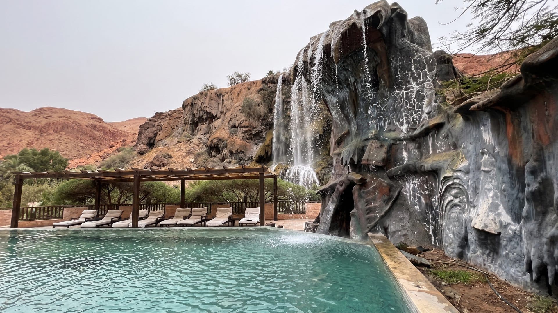 The hot waterfall at Ma'in falling down the dark rock face into the pool, with the timber pergola alongside