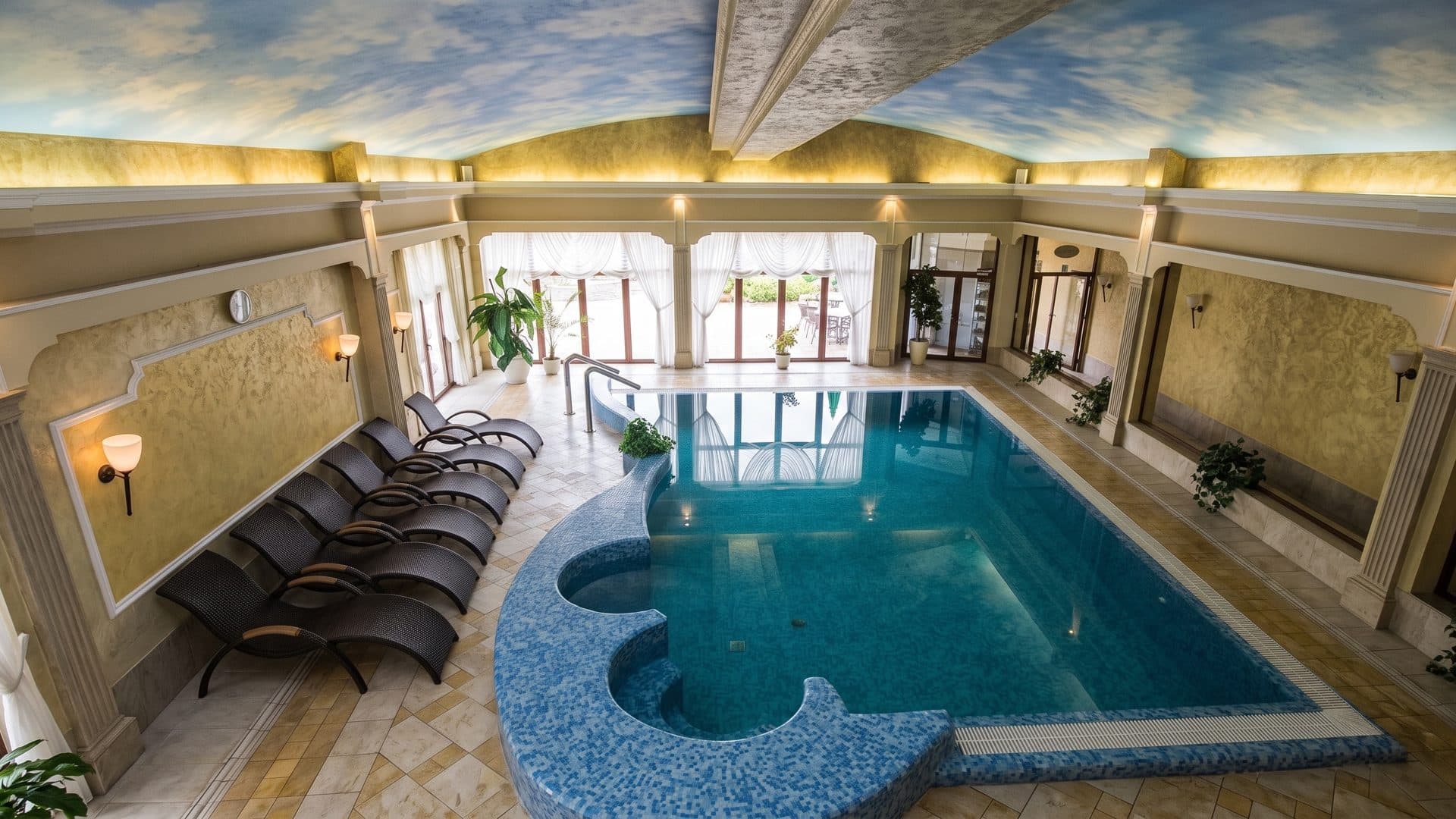 The indoor pool of Malinowy Zdroj with a mosaic whirlpool, loungers and a painted sky ceiling