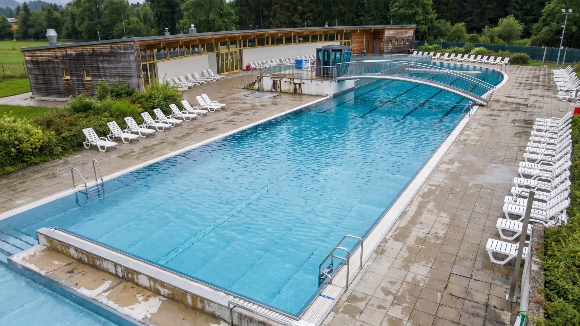 Outdoor thermal pool partly under a clear canopy, lined with white loungers, with the timber building behind