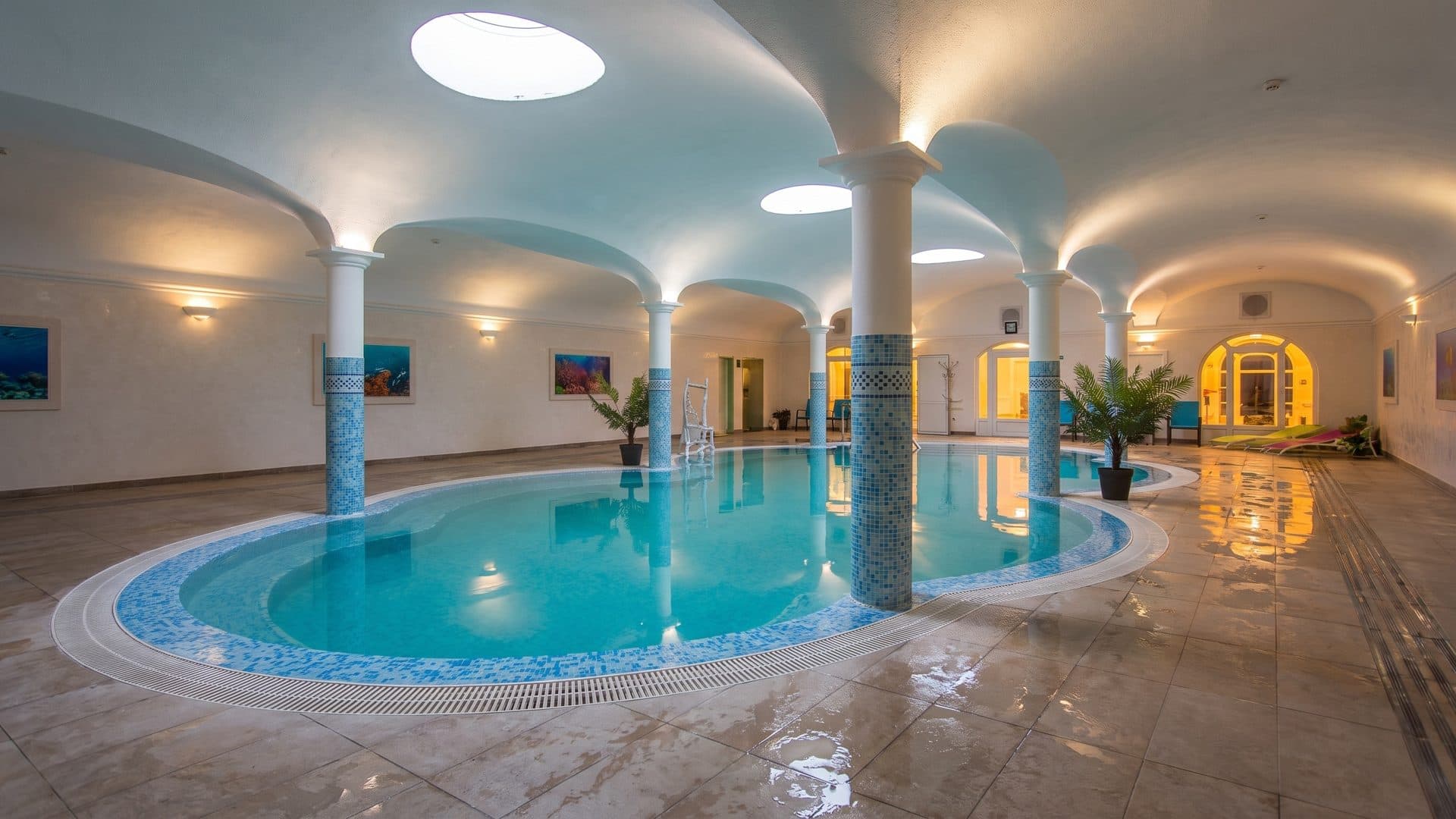 Indoor thermal pool in a white vaulted hall with tiled columns and round skylights