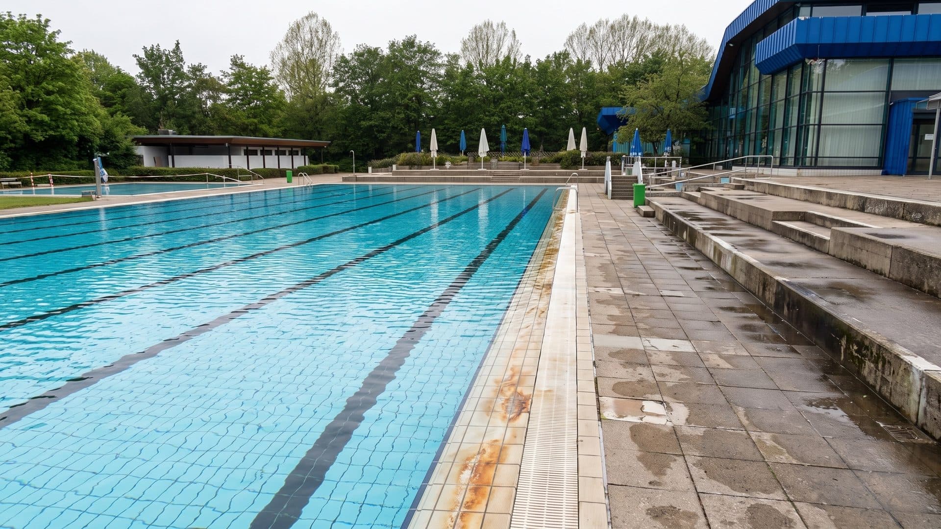Outdoor lap pool with long concrete terraces along one side and the blue-clad pool building