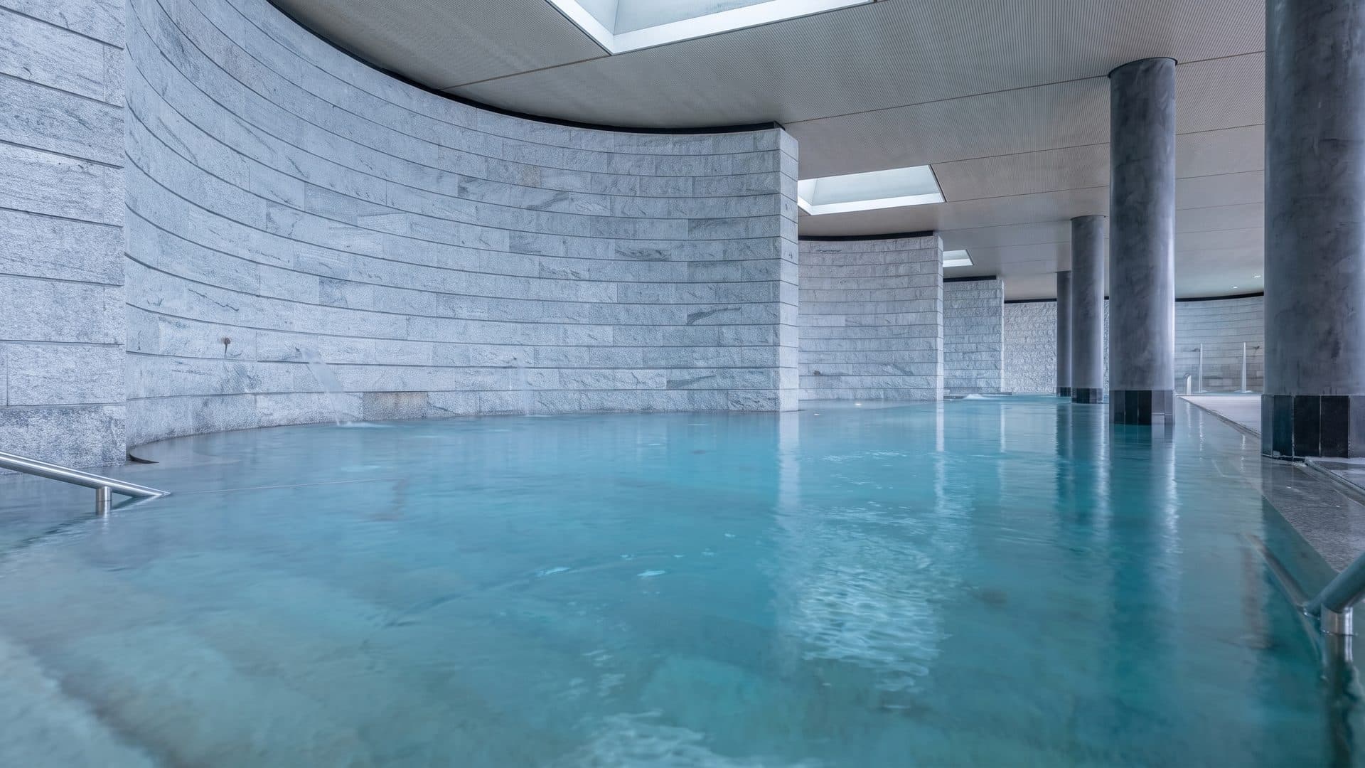The indoor mineral bath at Rigi Kaltbad: a curved dressed-stone wall above a still pale blue pool.