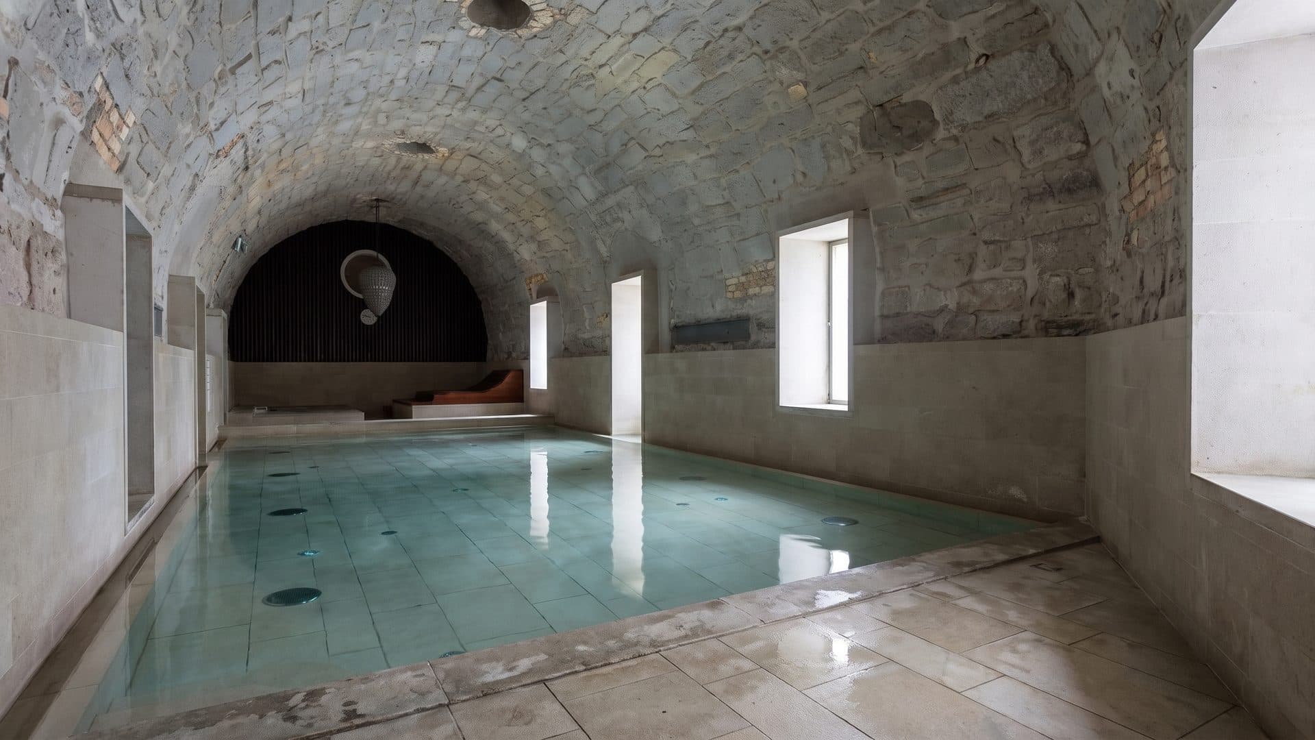 The vaulted stone bathing chamber of Mineralbad & Spa Samedan, shallow water running under the barrel vault.