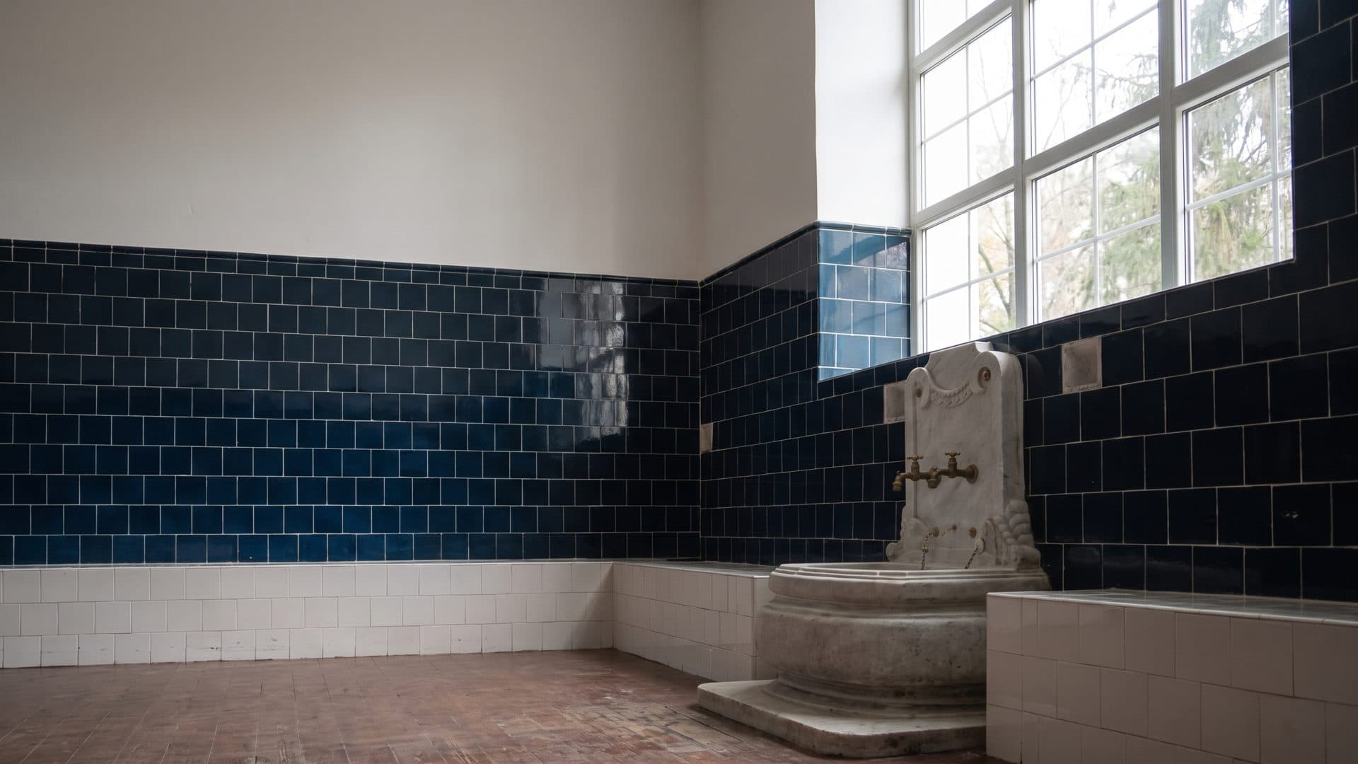 A blue-tiled hall of the mineral baths at Bankya with a carved stone spring basin against the wall and tall windows above it
