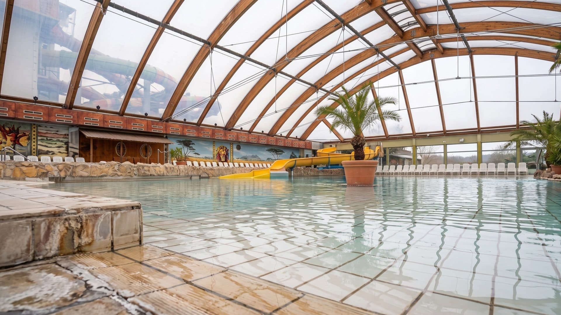 The leisure pool of the Miramar in Weinheim under a curved timber and glass roof, with palms and slides behind