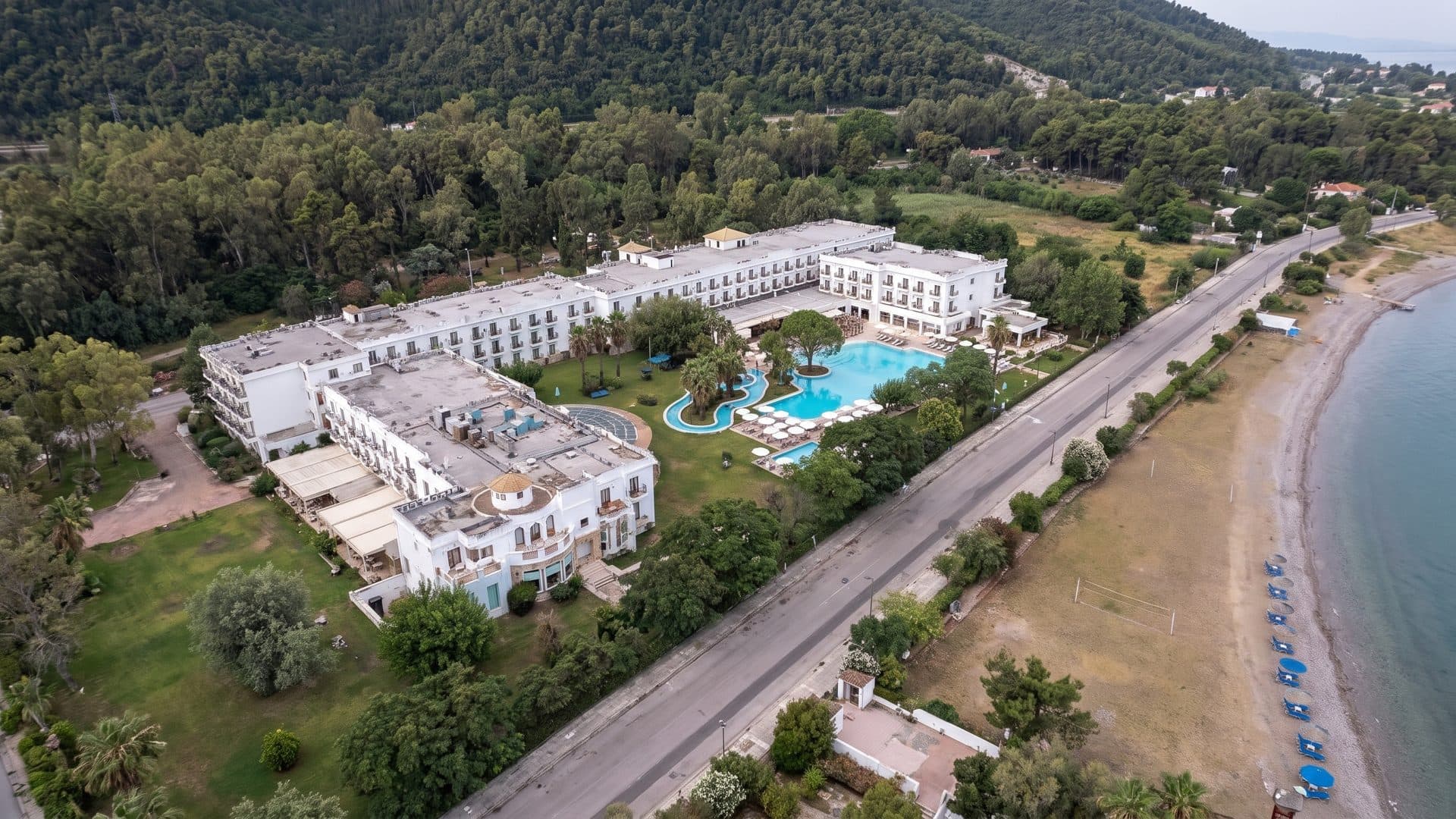 Mitsis Galini in Kamena Vourla from the air: the white hotel wings and their pool above the beach, with the pine hillside behind