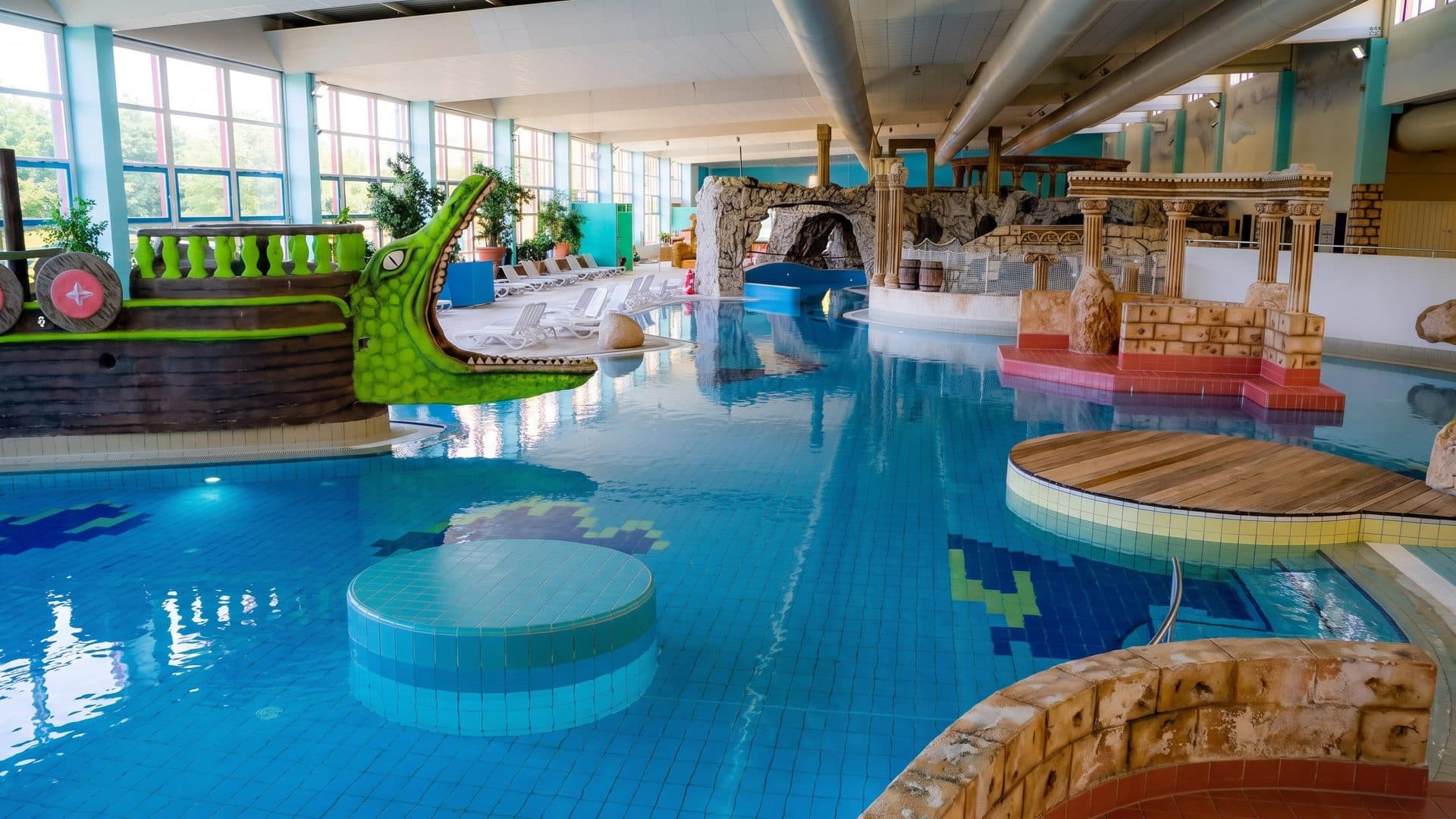 Indoor leisure pool with a green dragon boat, round stepping platforms and themed stone structures