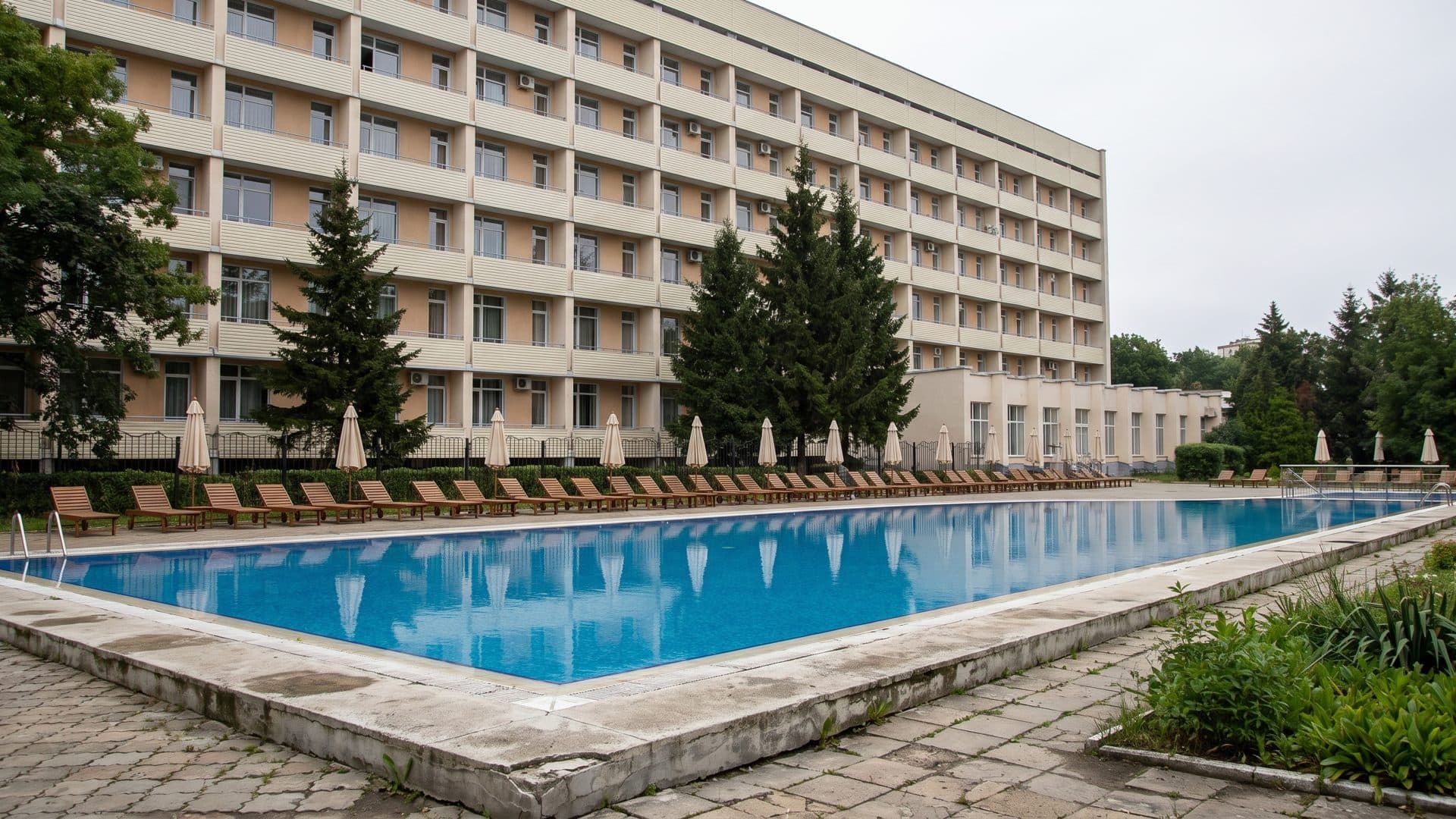 The long outdoor pool at Myrhorodkurort below the sanatorium block, with loungers and folded umbrellas along its edge