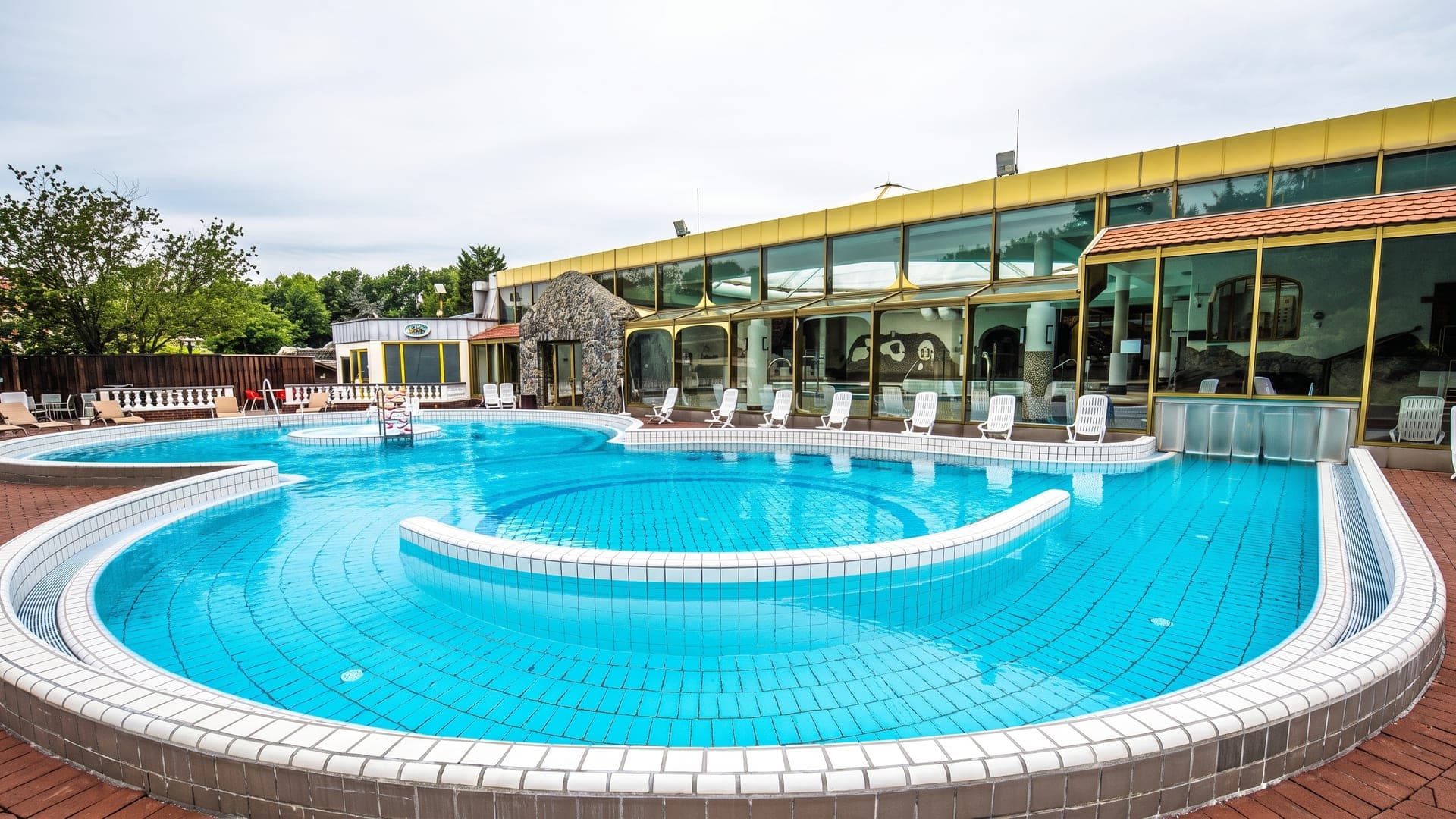 The outdoor pool at the Niederrhein-Therme in Duisburg, its curved edge in front of the yellow-framed hall.