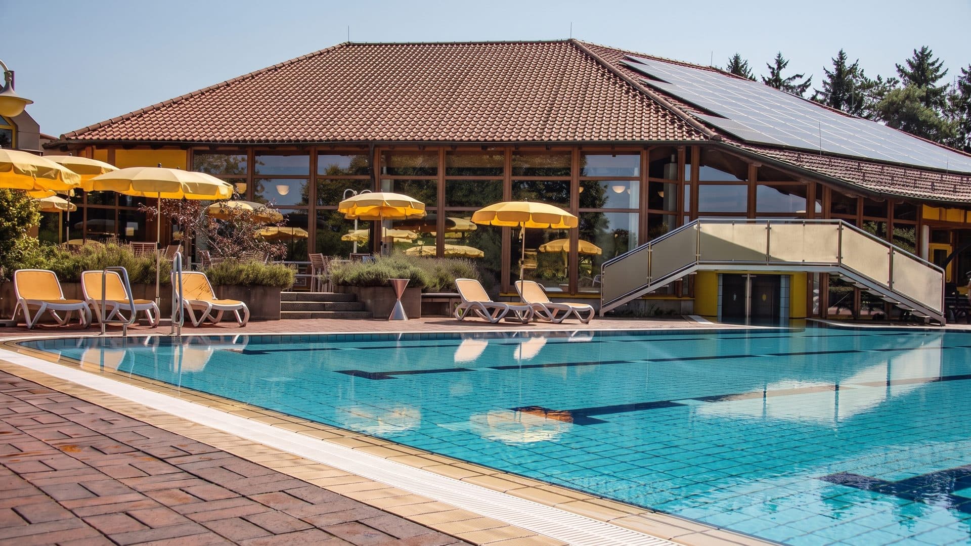 The outdoor pool of the Novamare in front of its bath building under the yellow umbrellas