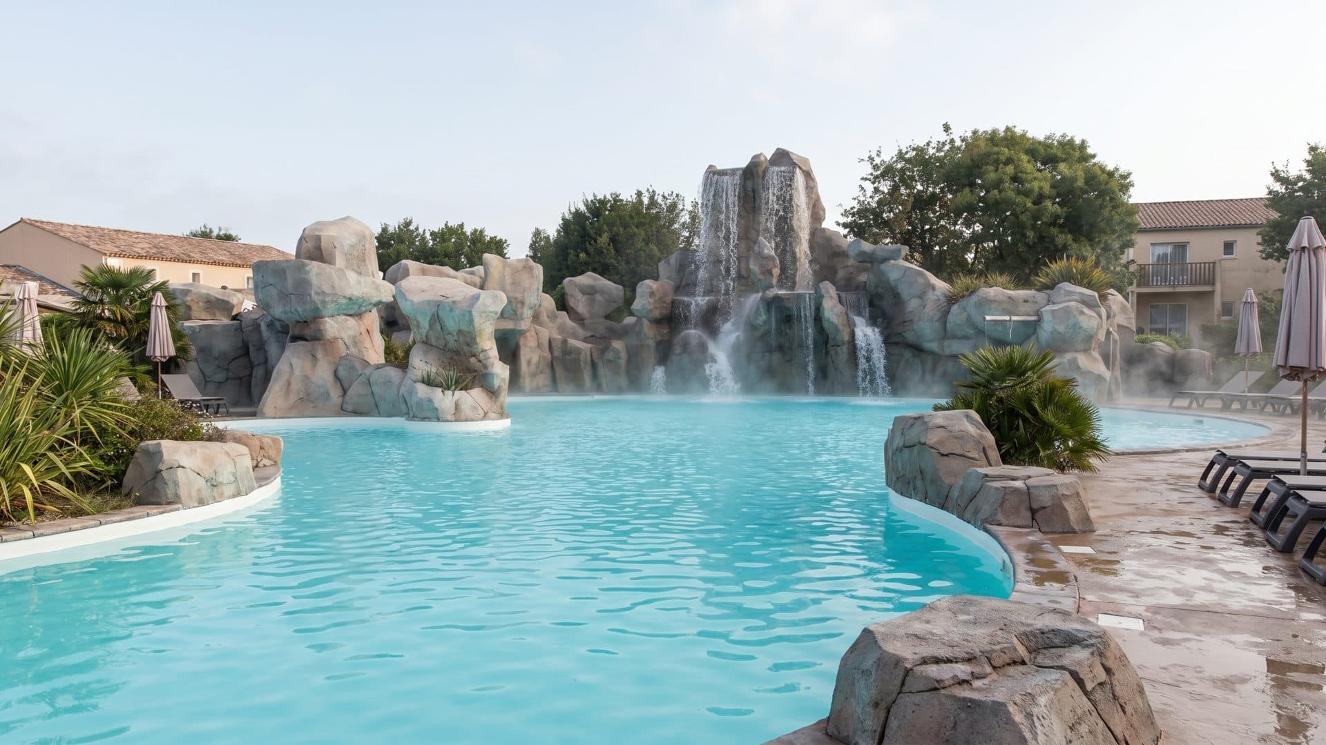 The rock-walled lagoon at O'Gliss Park with waterfalls spilling over boulders into turquoise water, planting along the banks