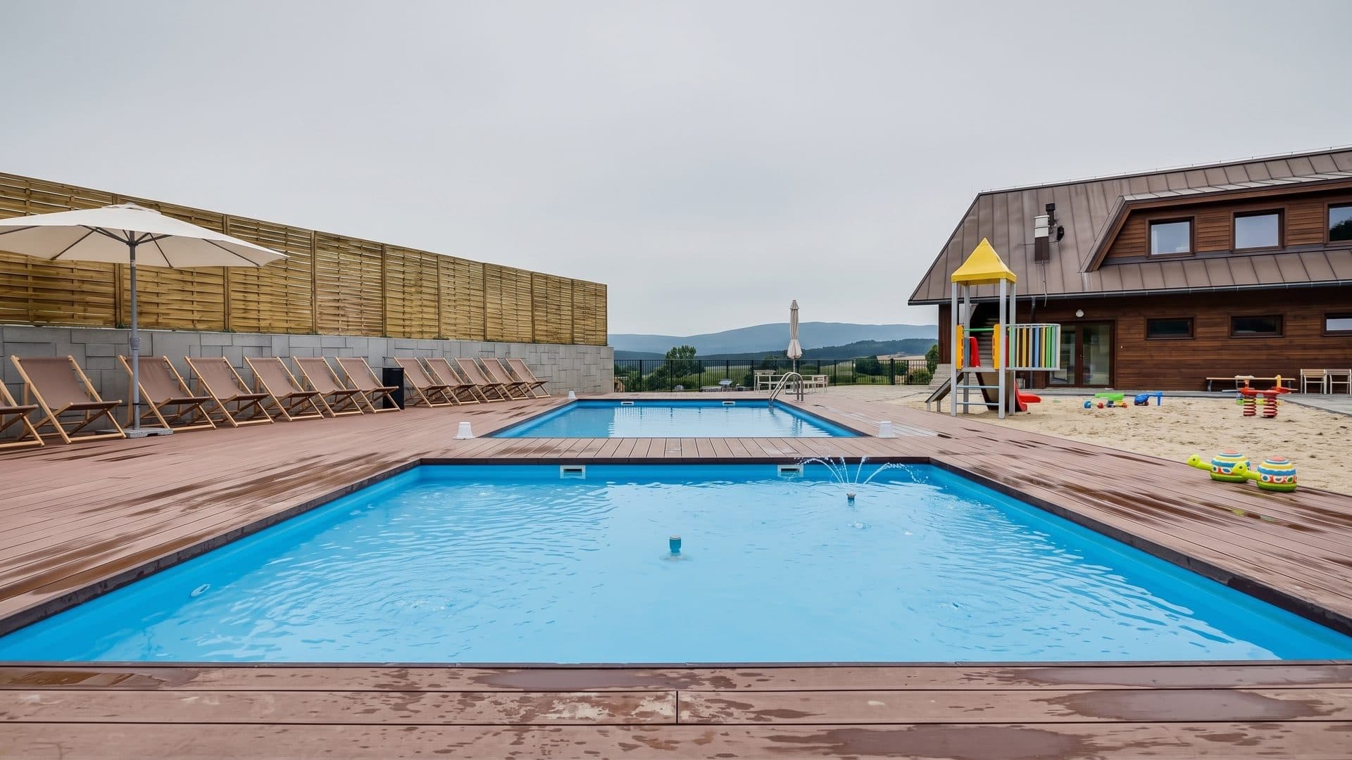 The outdoor pools of Osada Sniezka in Karpacz on a timber deck with loungers and a children's tower