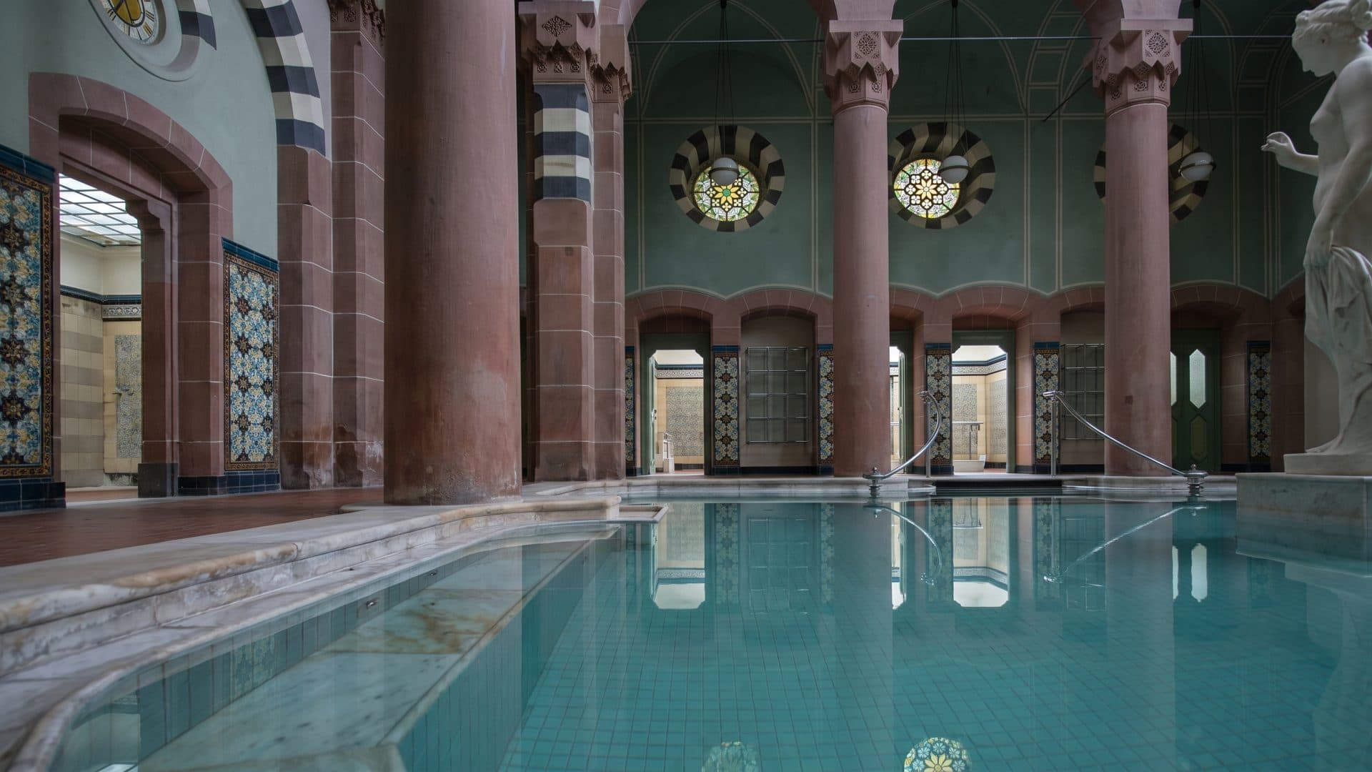 The Moorish bathing hall of the Palais Thermal, its pool running between tiled columns with a marble figure at the far end