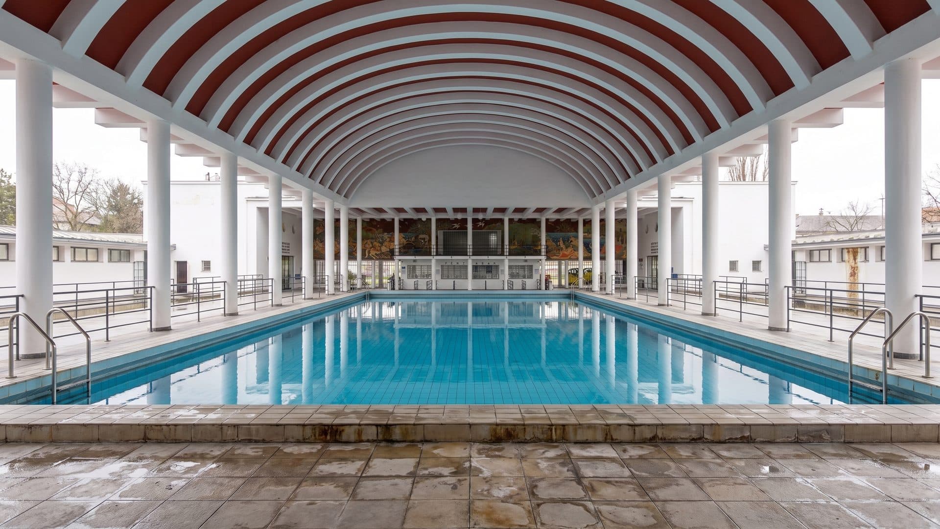 The indoor hall of the Palatinus baths under its red and white striped barrel vault, the pool full and painted galleries along both sides