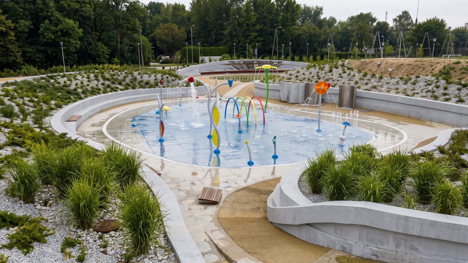 The outdoor splash pad of Park Wodny Planty with coloured water sprays among grasses and gravel beds