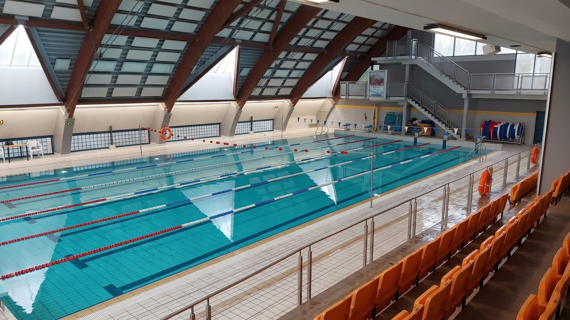 The competition pool in Swidwin seen from the stands with orange seats, under a sawtooth roof