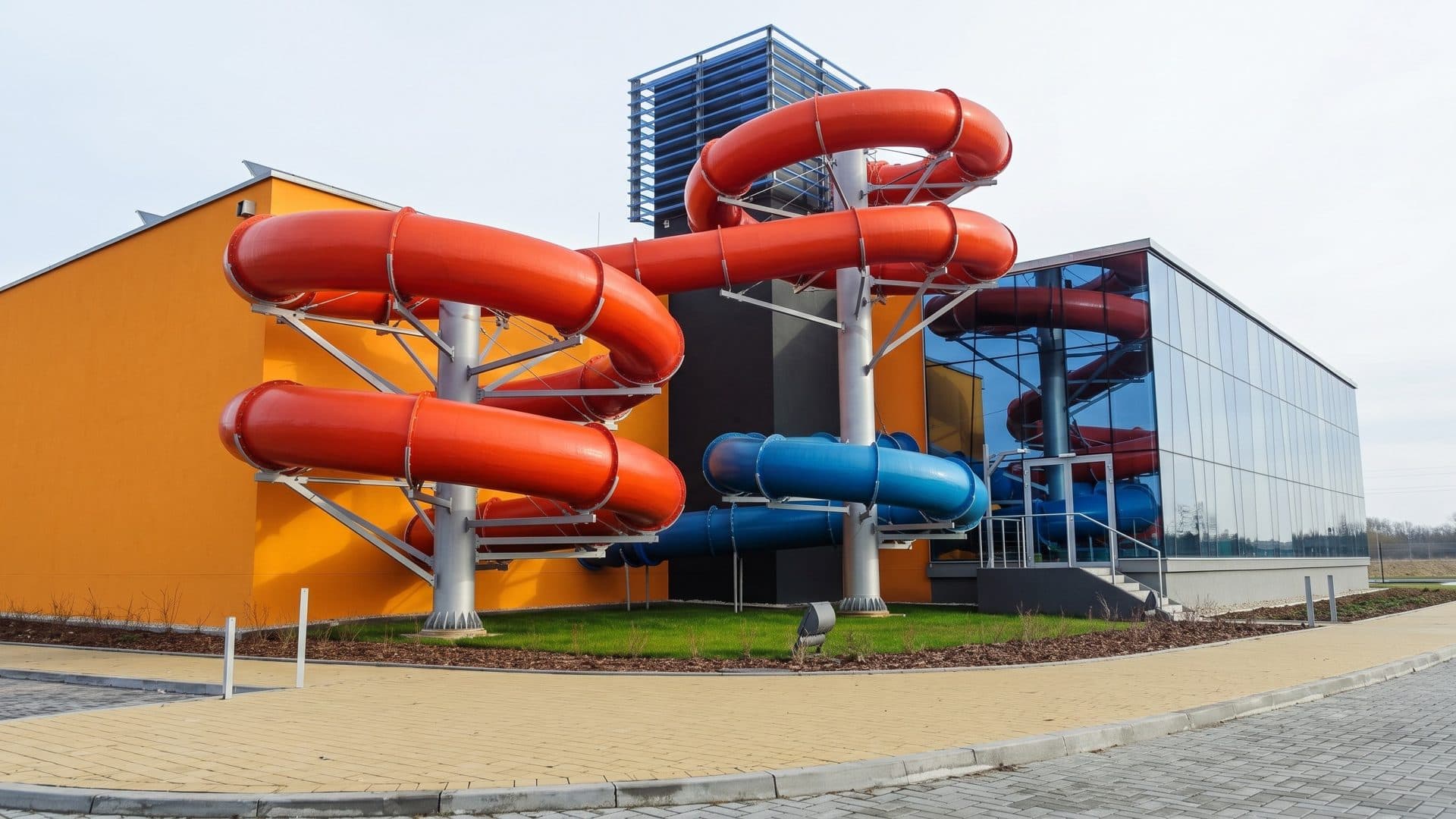 Red and blue slides looping outside the orange and glass building of Park Wodny Siedlce