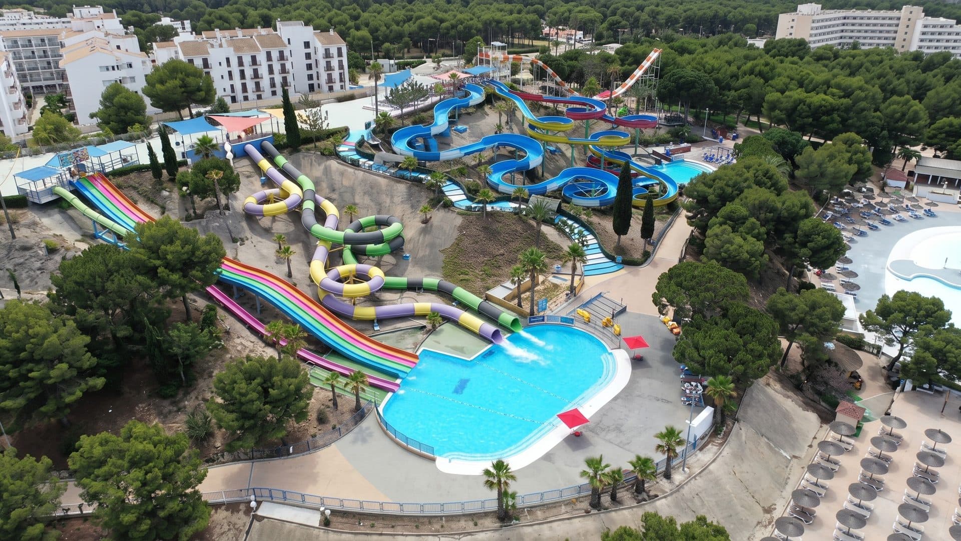 Aerial view of the AquaVera water park: coloured slides running down to a curved pool among pine trees