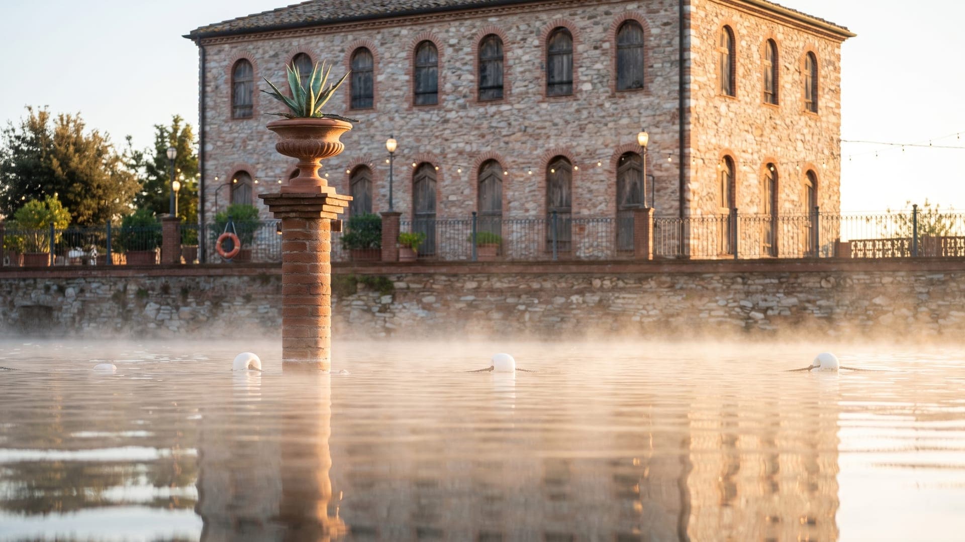 Steaming thermal lake at dawn in front of a stone industrial building