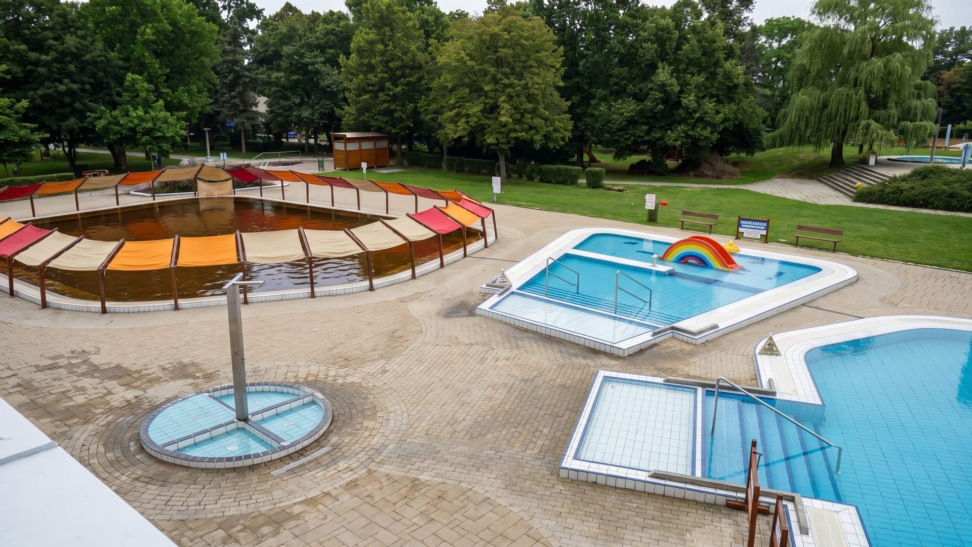 Outdoor children's pools with a rainbow feature and a colourful shaded seating ring in a park