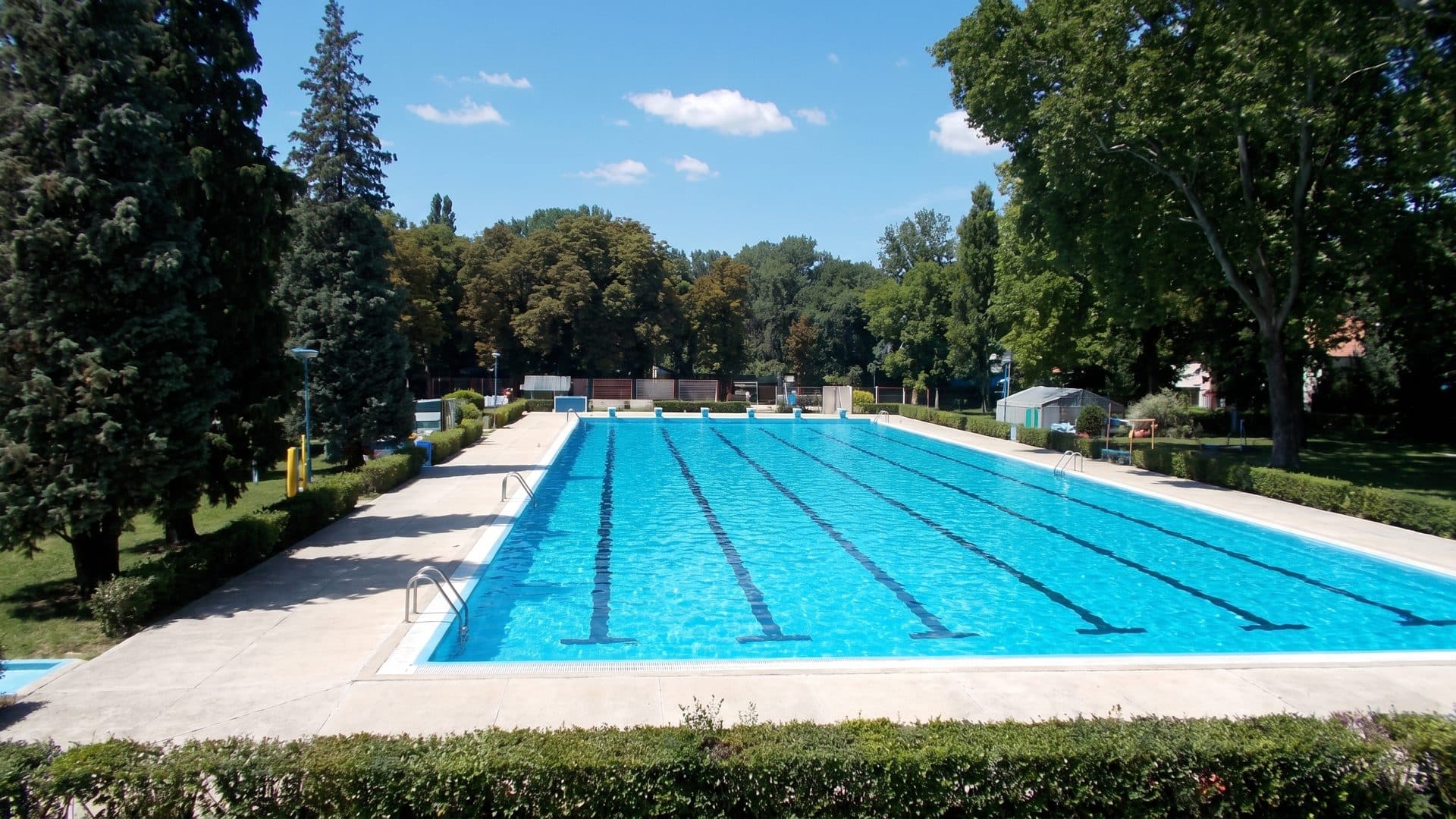 The outdoor lap pool of the Pünkösdfürdő baths stretching across its lawn between the park trees