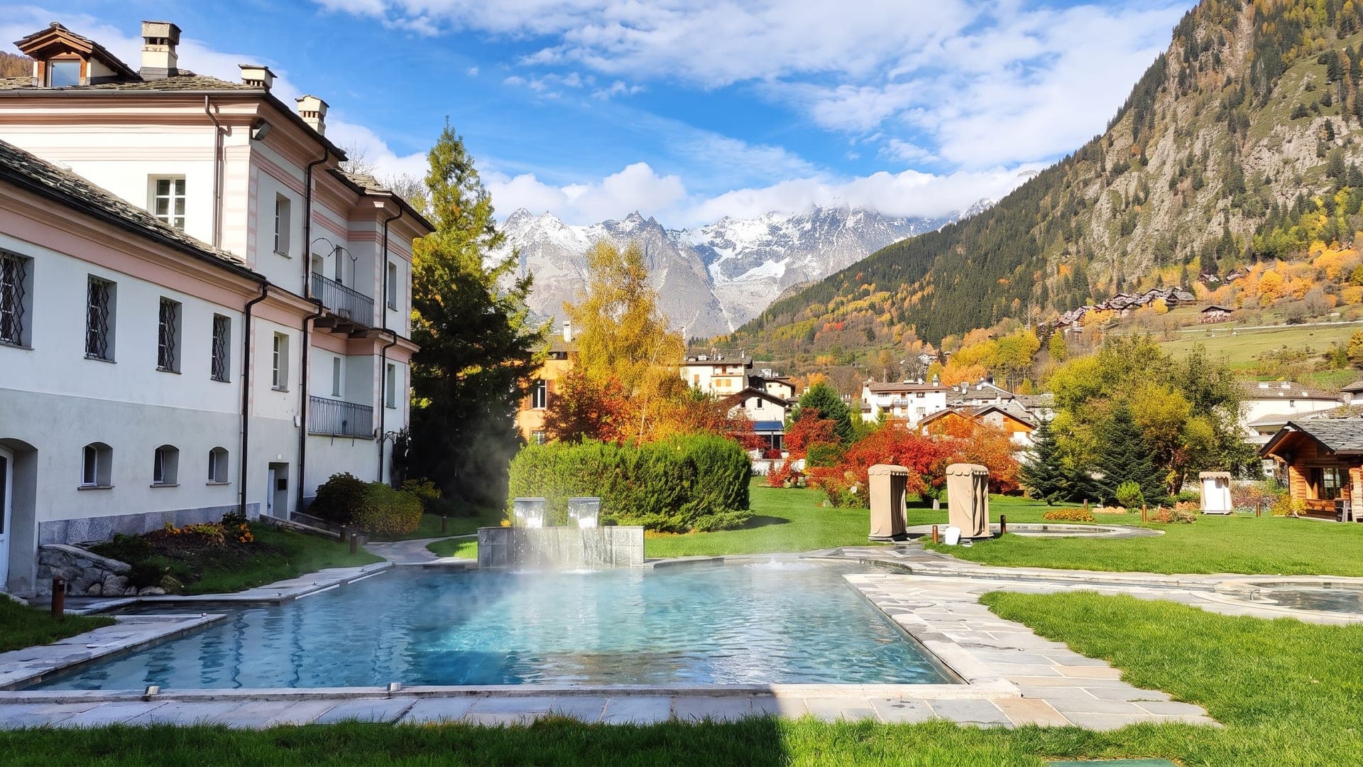 The outdoor pool at QC Terme Pre Saint Didier in autumn, steam rising with the snow-capped Alps beyond.