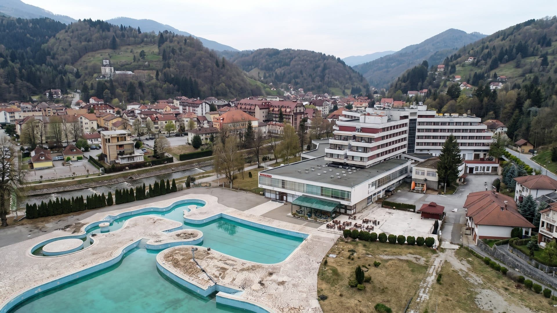 The free-form outdoor pools of Reumal in Fojnica from the air, with the terraced town and wooded hills behind them