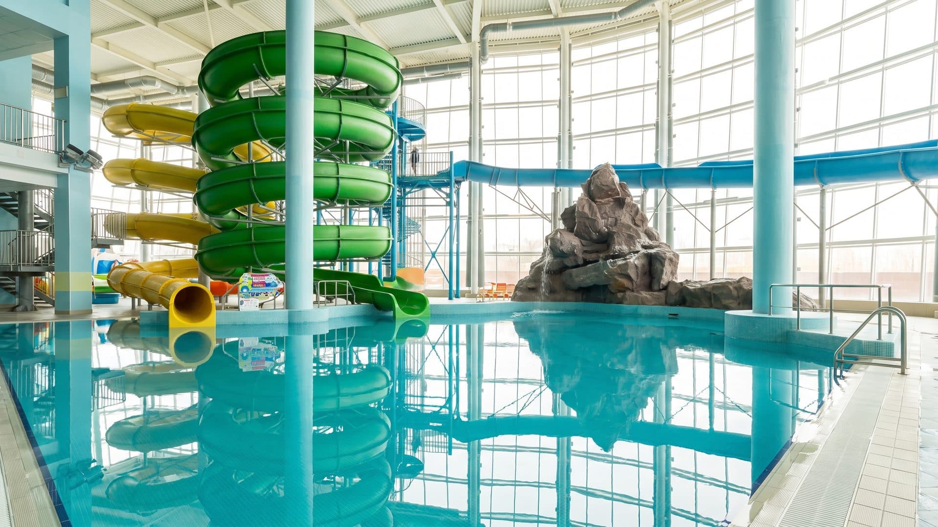 The green and yellow slide tower of Rodeo Drive standing above the pool in its glazed hall