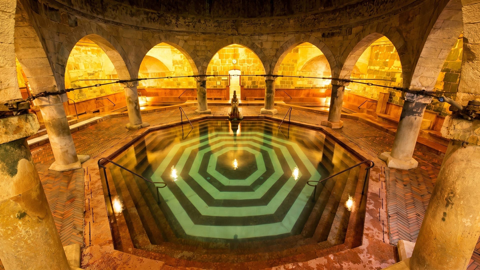 The Turkish bathing hall at the Rudas bath in Budapest, its octagonal pool between stone columns under warm lamplight.