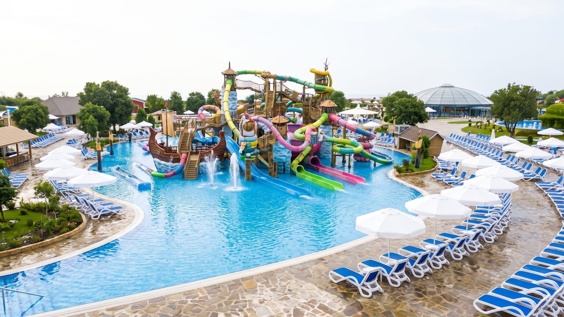 The outdoor lagoon at Rulantica below a timber pirate-ship play structure, with rows of blue loungers along the pool