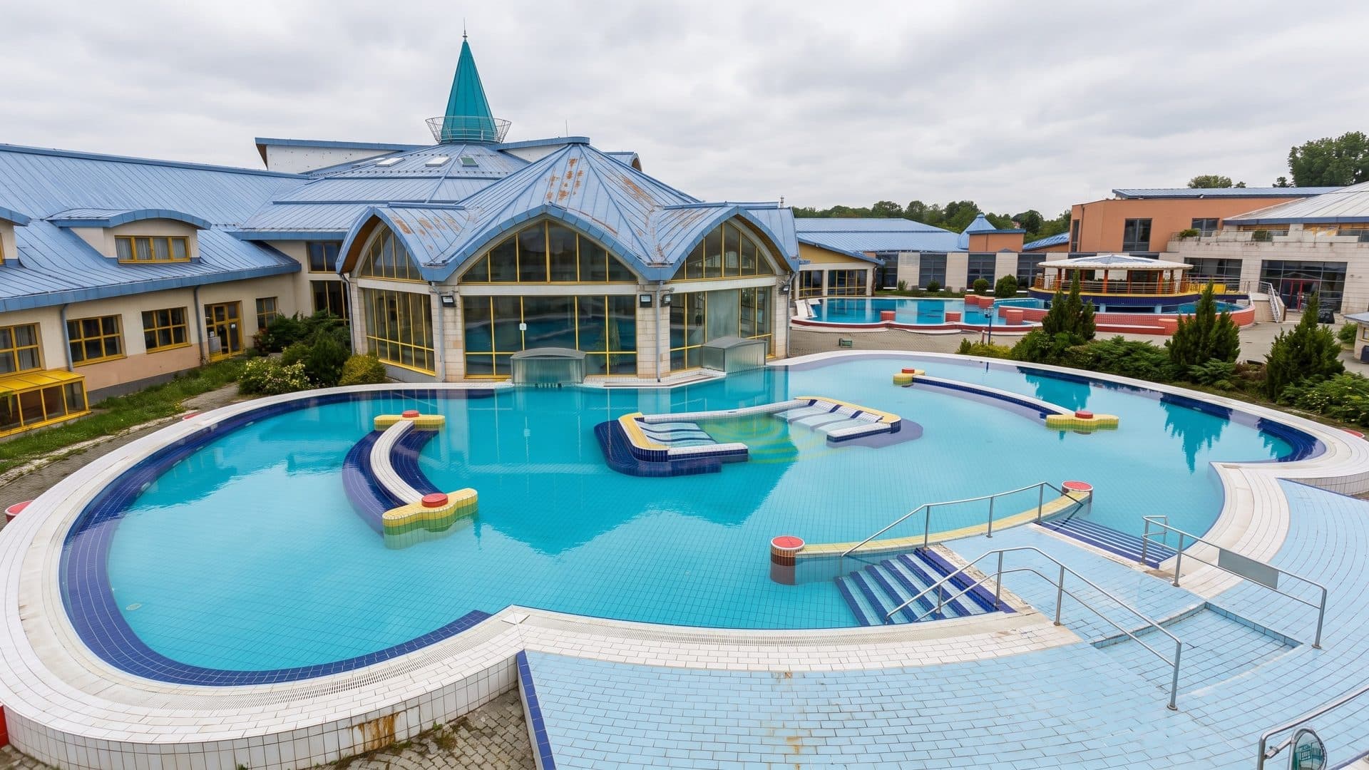 Outdoor thermal pool with lounging islands in front of the blue-roofed bath with its glass pyramid spire