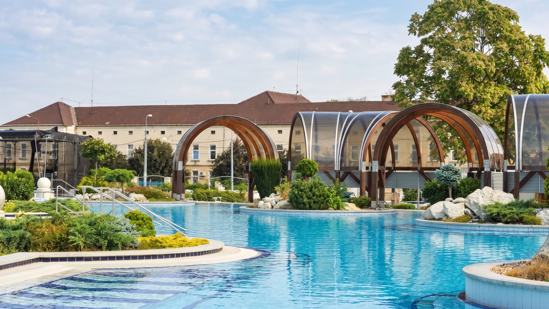 The outdoor pool at the Selyemret lido in Miskolc, in front of arched timber pavilions.