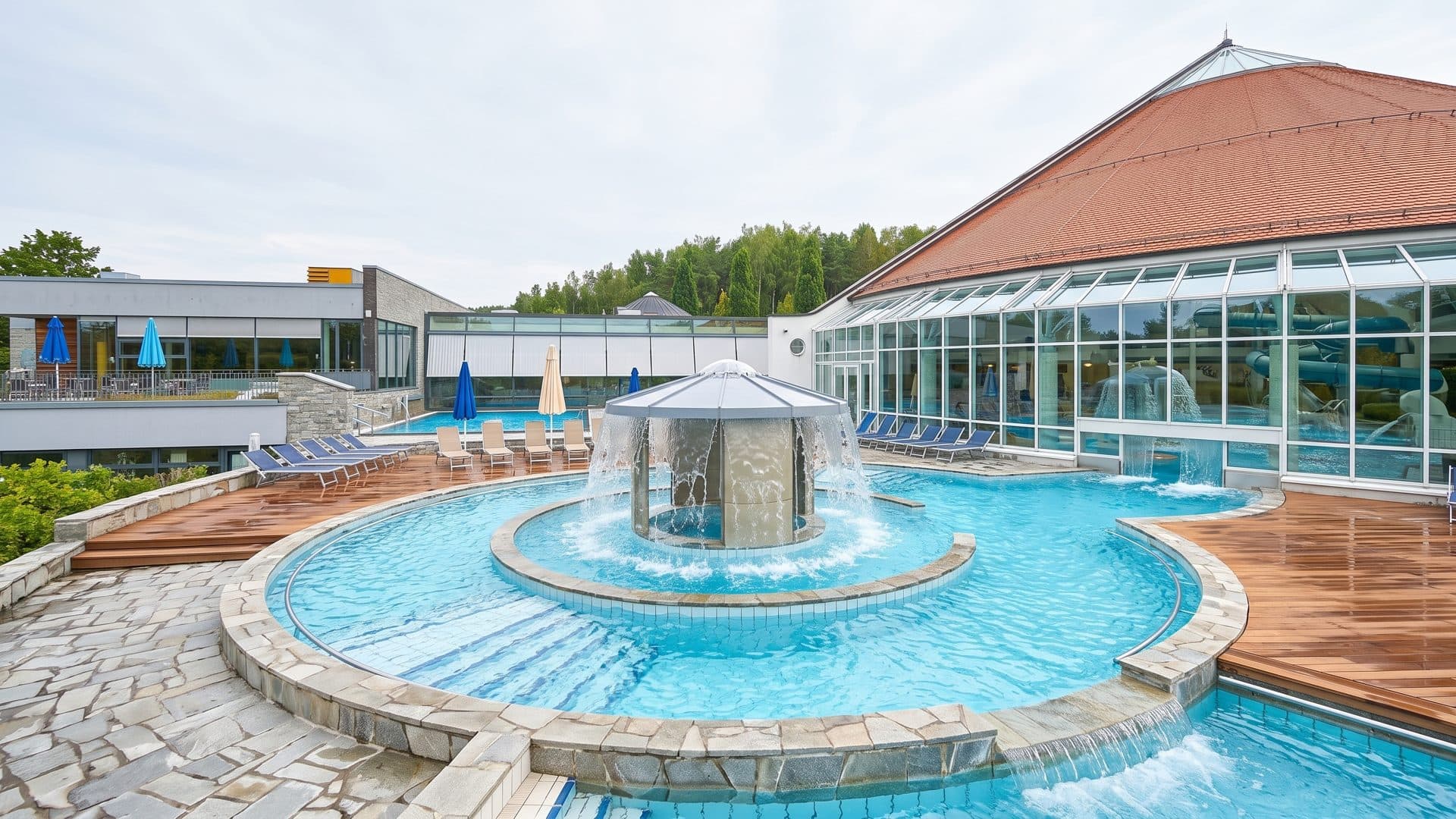 The baths seen from above: the orange tent roof over the glass hall, with the round outdoor pool and its fountain below.