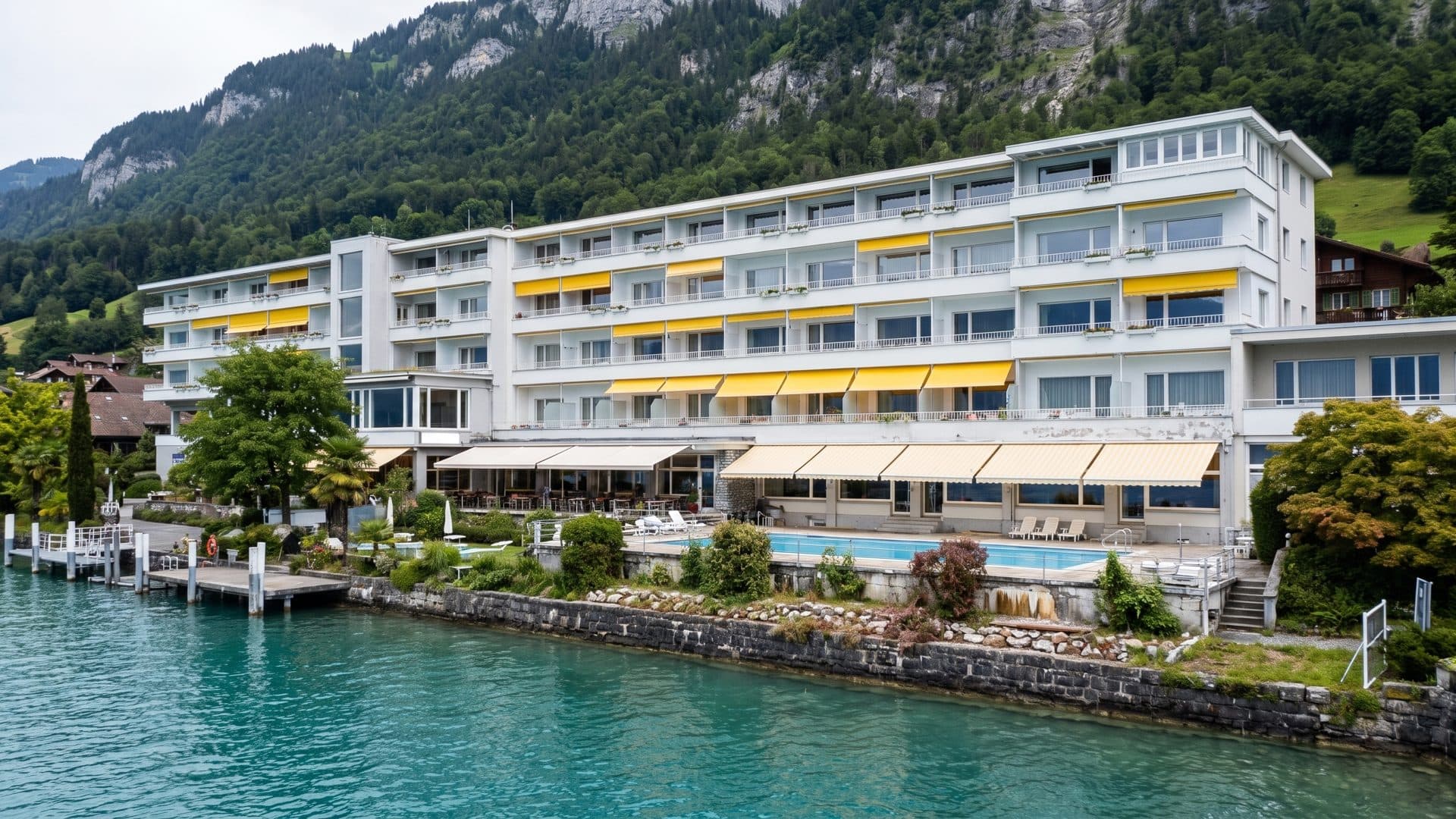 The SOLBAD Beatus seen from Lake Thun, its balconied wings above the lakeside terrace and outdoor pool, with wooded cliffs rising behind