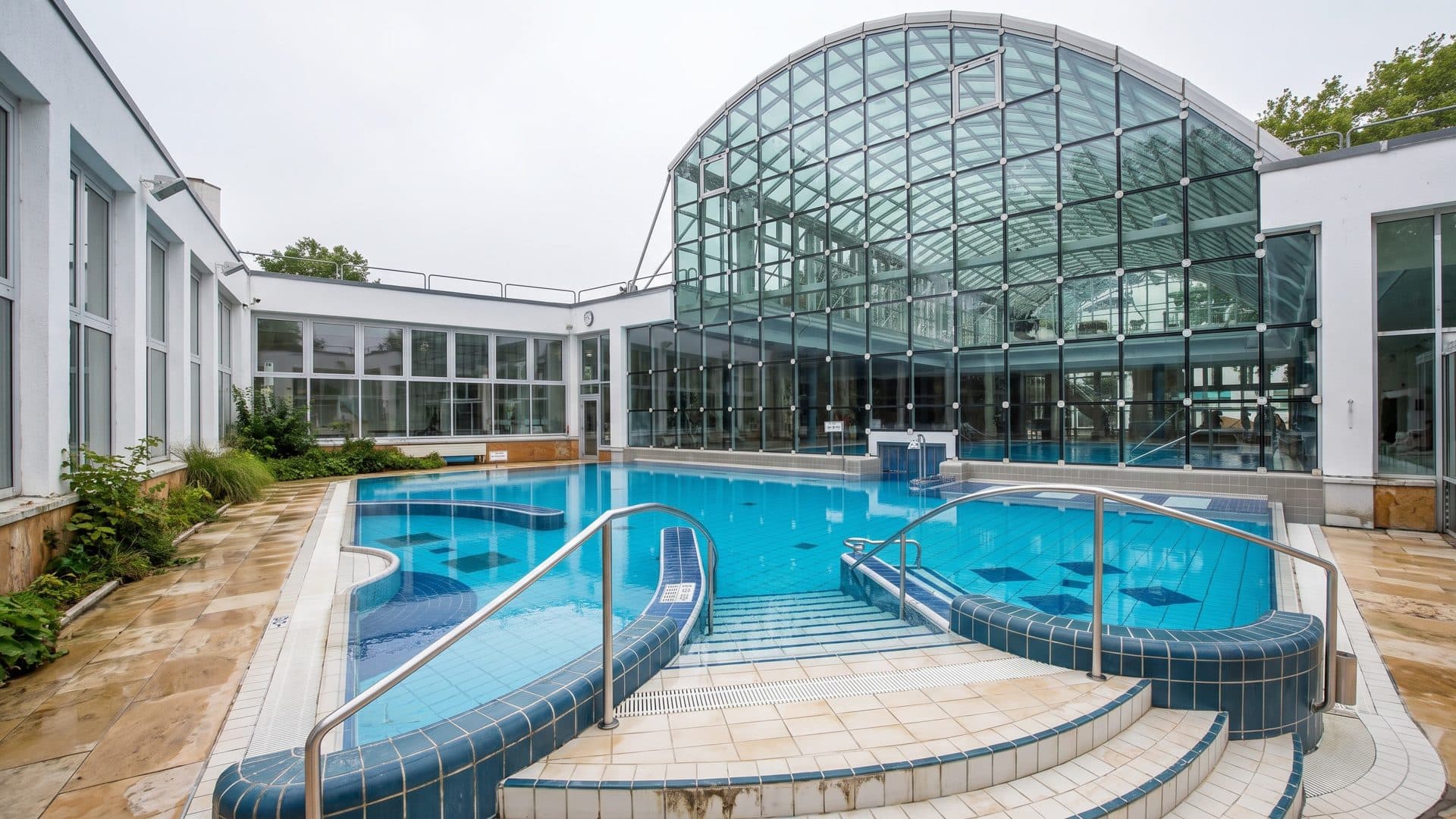 Outdoor brine pool with curved tiled benches and steps, in front of the arched glass hall