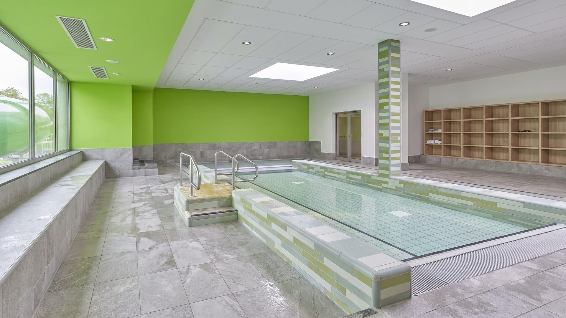 Shallow indoor brine pool with stepped entry and handrails, in a bright room with a lime-green wall
