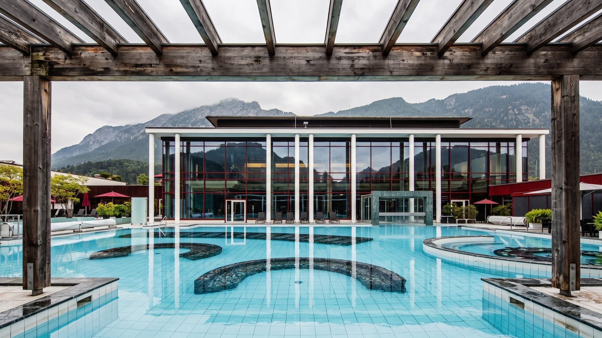 The outdoor pool at the Rupertustherme under its timber pergola, with a mountain ridge rising behind